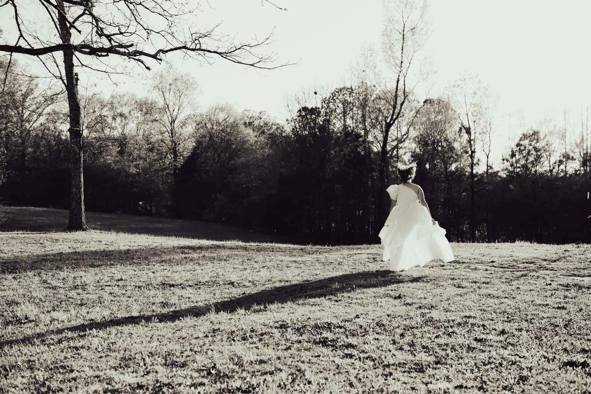 Black and white senior portrait of girl running in dress through Alabama field, Darling Dear Photo