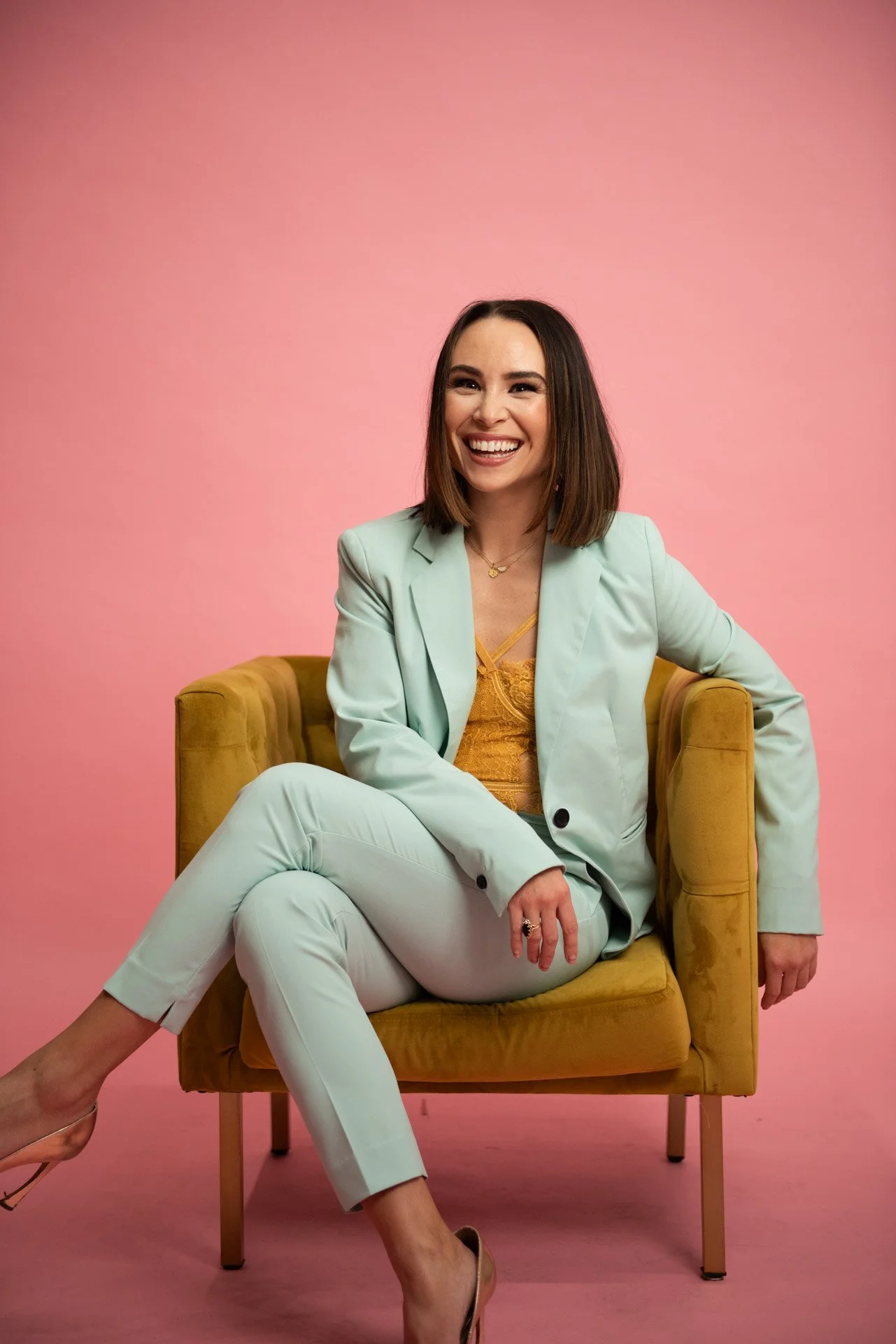 personal brand session of Tonia in light teal suit with pink backdrop and velvet mustard chair