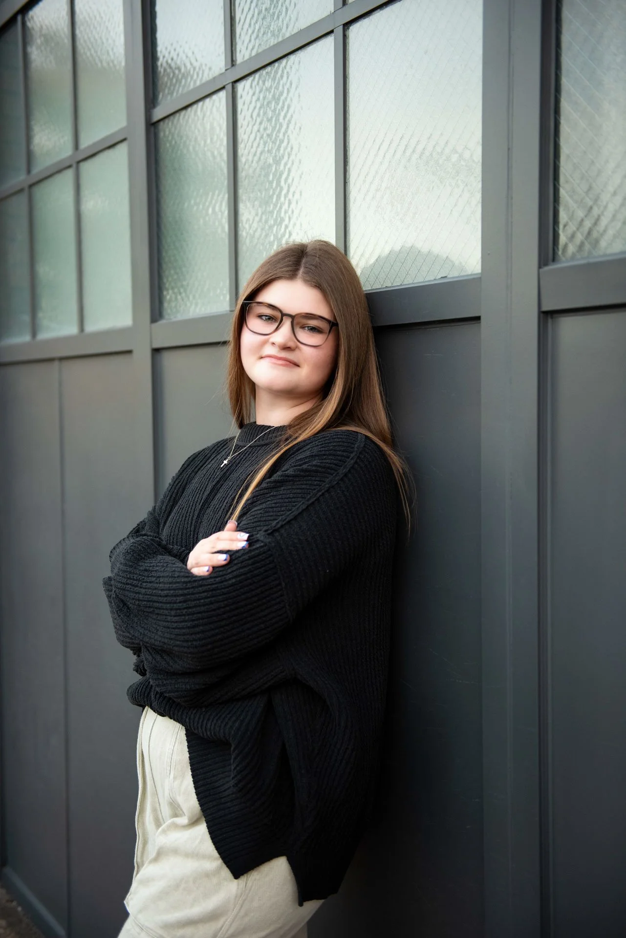 High school senior in black sweater arms crossed leaning against dark industrial door in Birmingham Alabama, Darling Dear Photo
