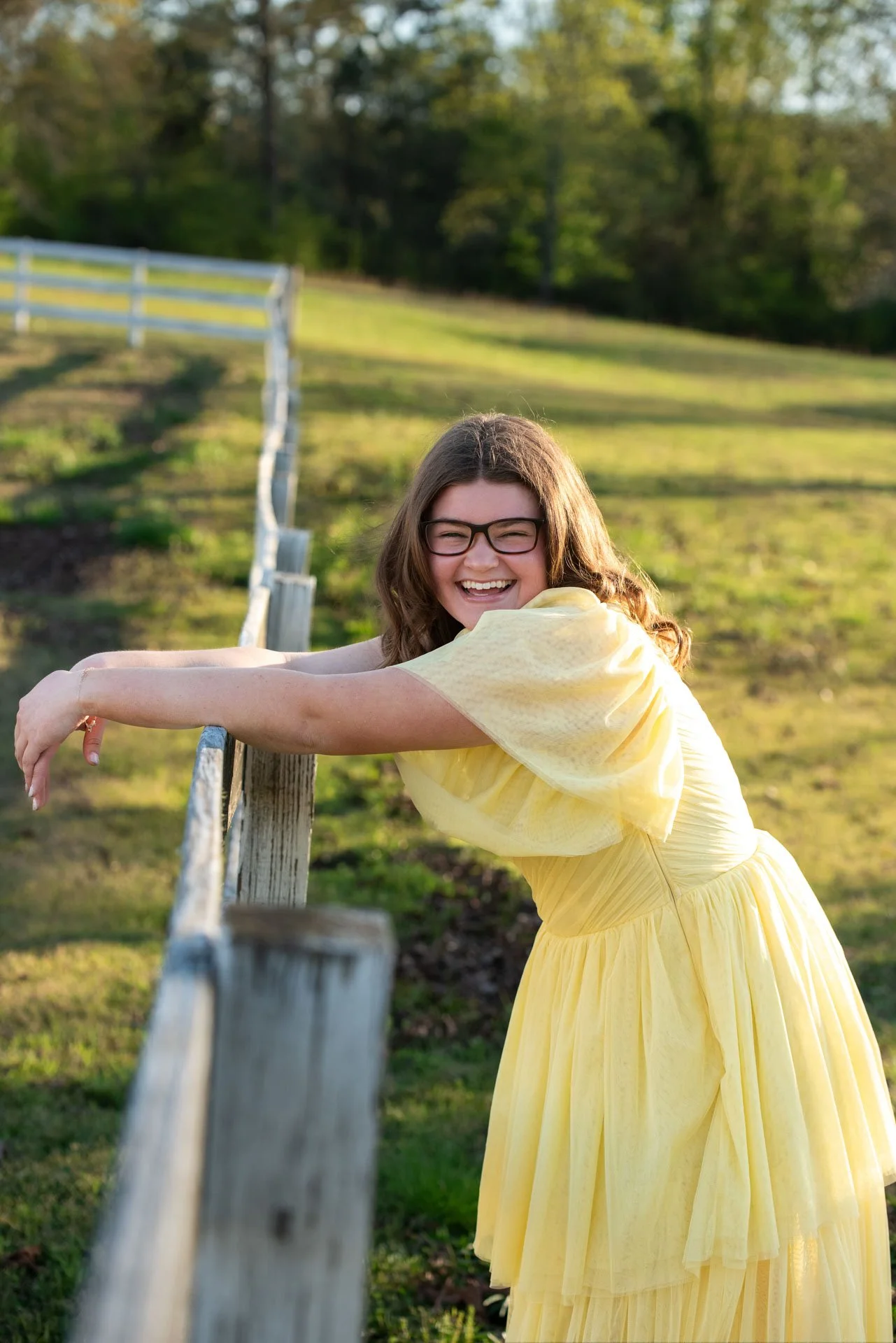 Senior girl in yellow dress laughing at wooden fence in Pell City Alabama field, Darling Dear Photo