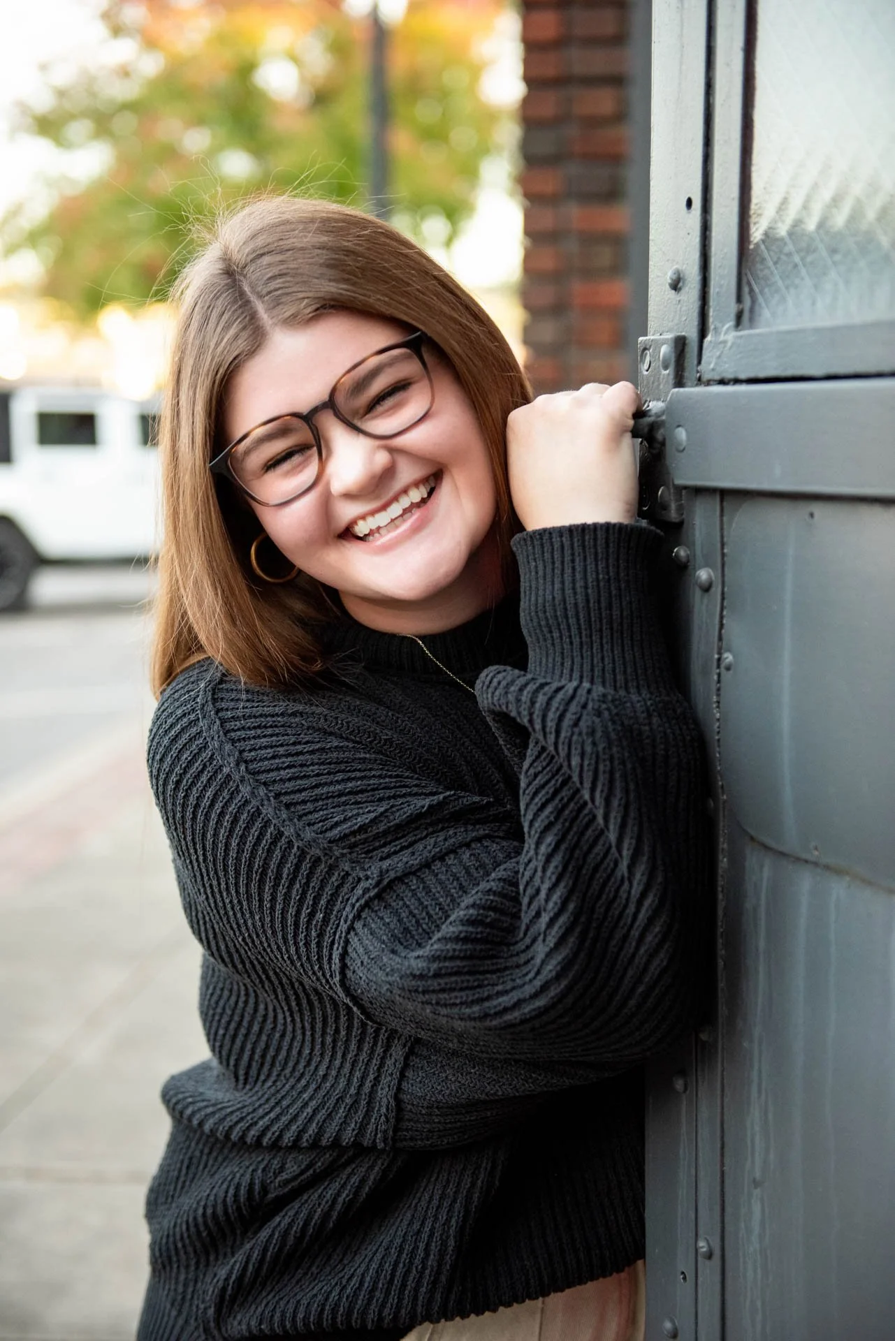 Senior girl in black sweater laughing while leaning on industrial door in Birmingham Alabama, Darling Dear Photo
