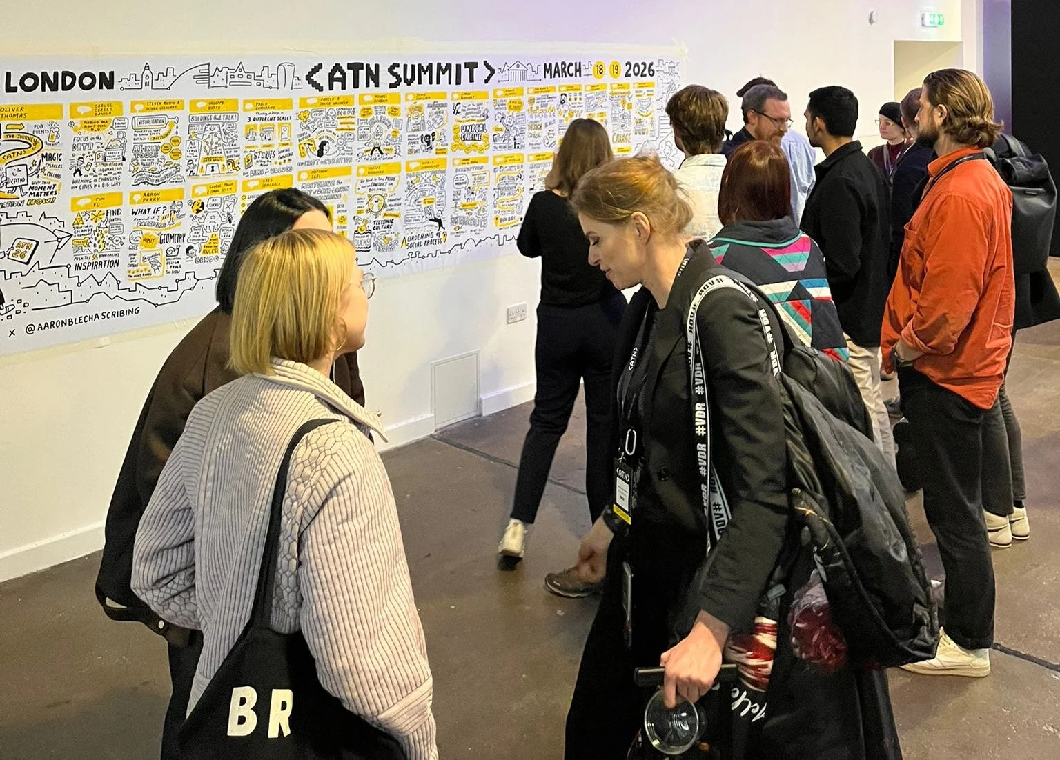 People gathered around an illustrated timeline of the KATN Summit held in London on March 18-19, 2026, displayed on a wall.