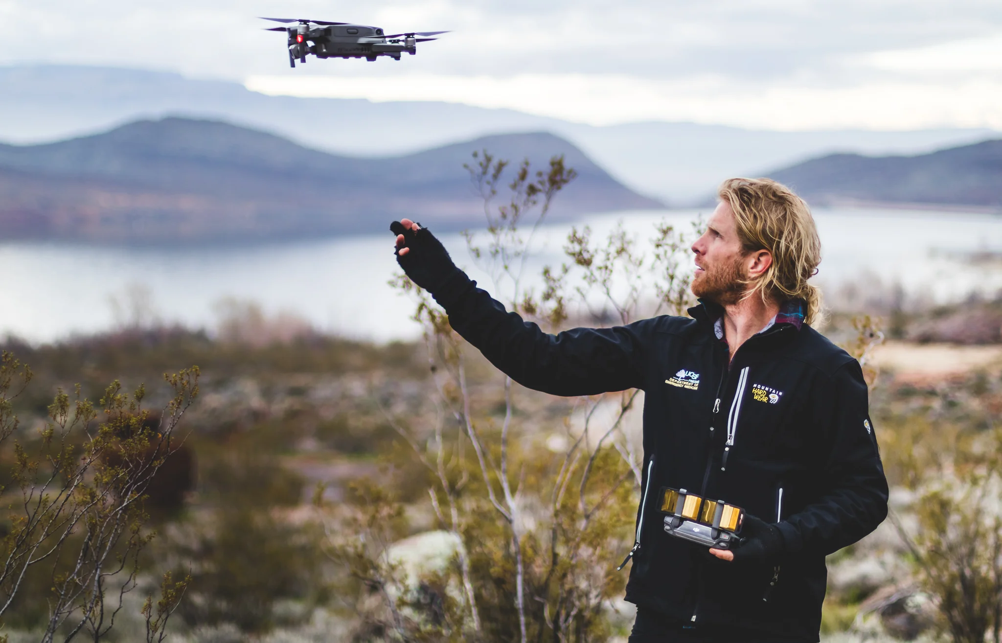 A man flying a drone outdoors in a scenic, mountainous landscape with a lake in the background