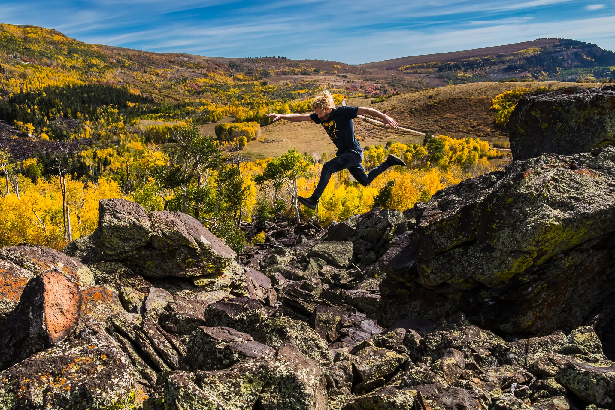 A person jumping between rocks in a mountainous landscape during autumn with yellow and green trees.