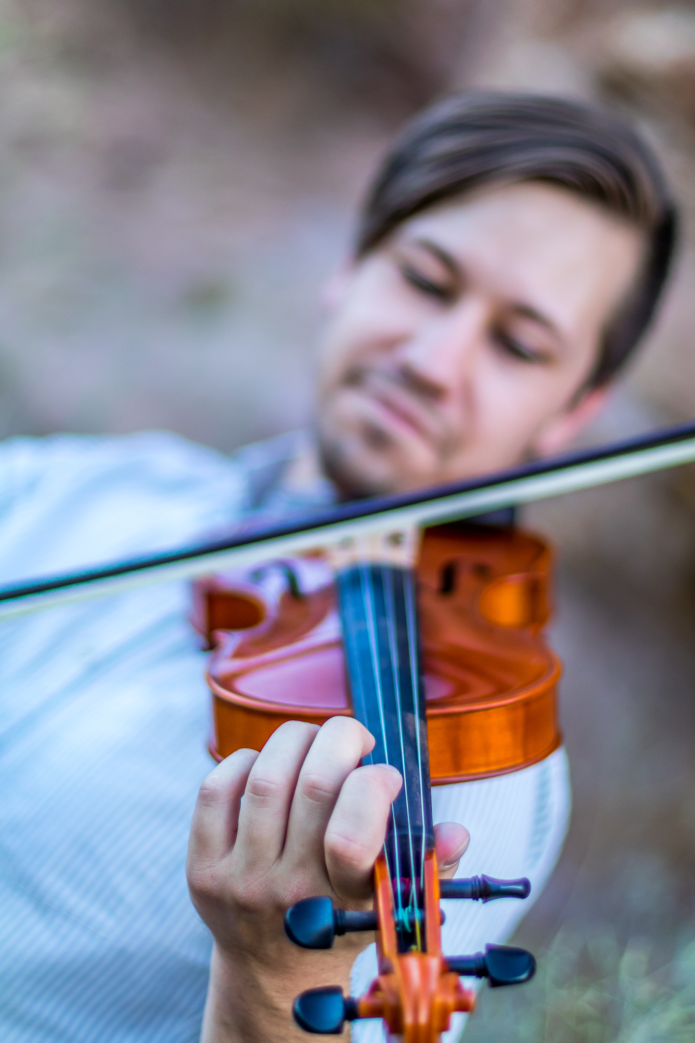 A young man playing the violin outdoors, focusing on the instrument with his eyes closed.
