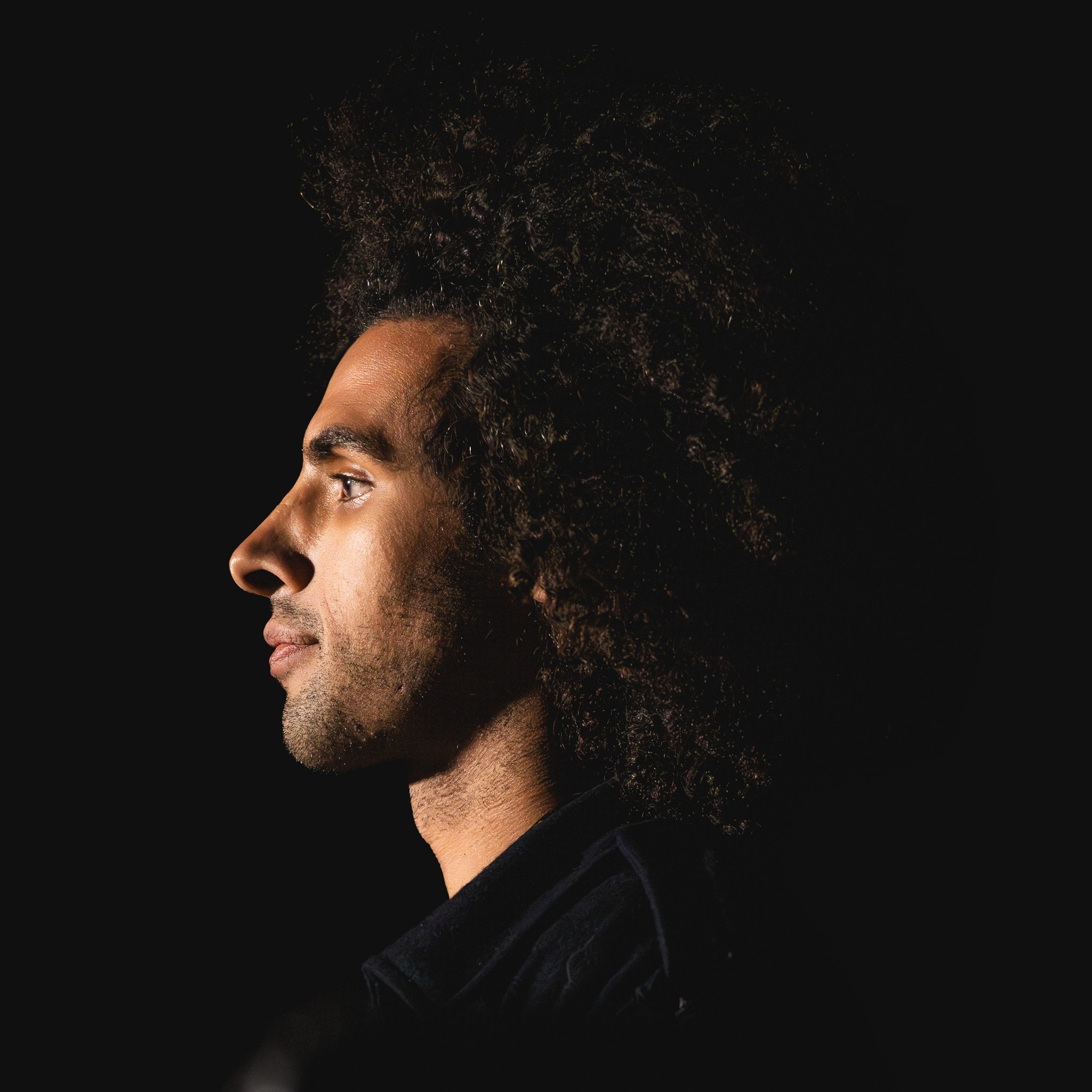 Profile of a man with curly hair against a black background.