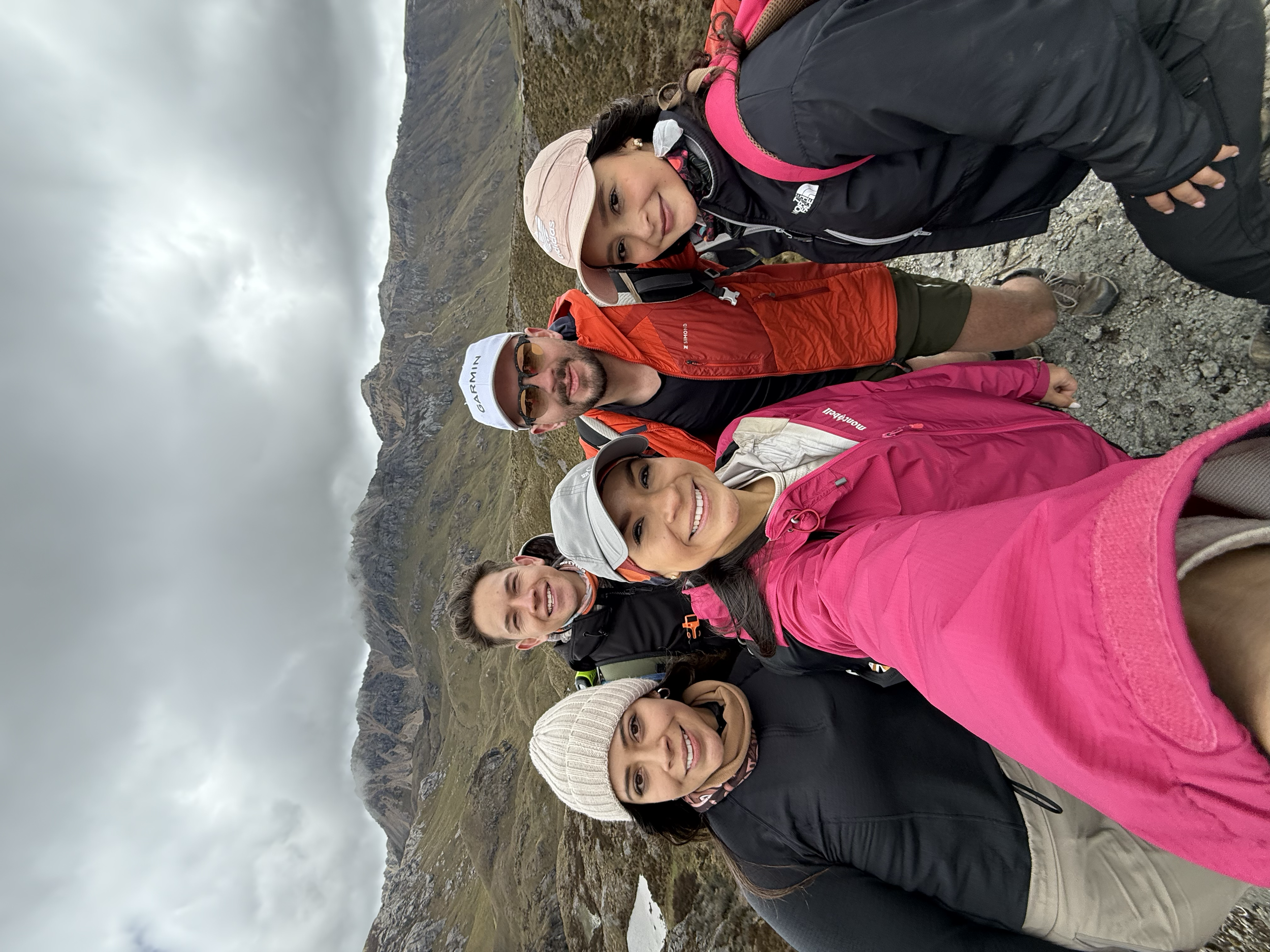 Grupo de cinco personas haciendo senderismo en una zona montañosa, con ropa de abrigo y mochilas, en un día nublado.
