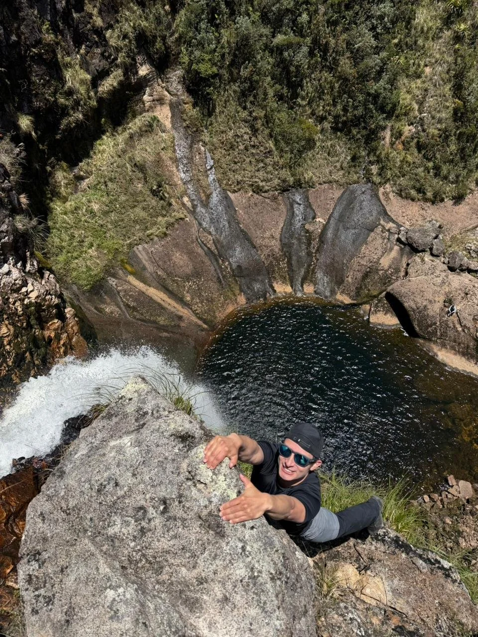 Persona haciendo rappel en una cascada en un entorno natural de montañas y árboles.