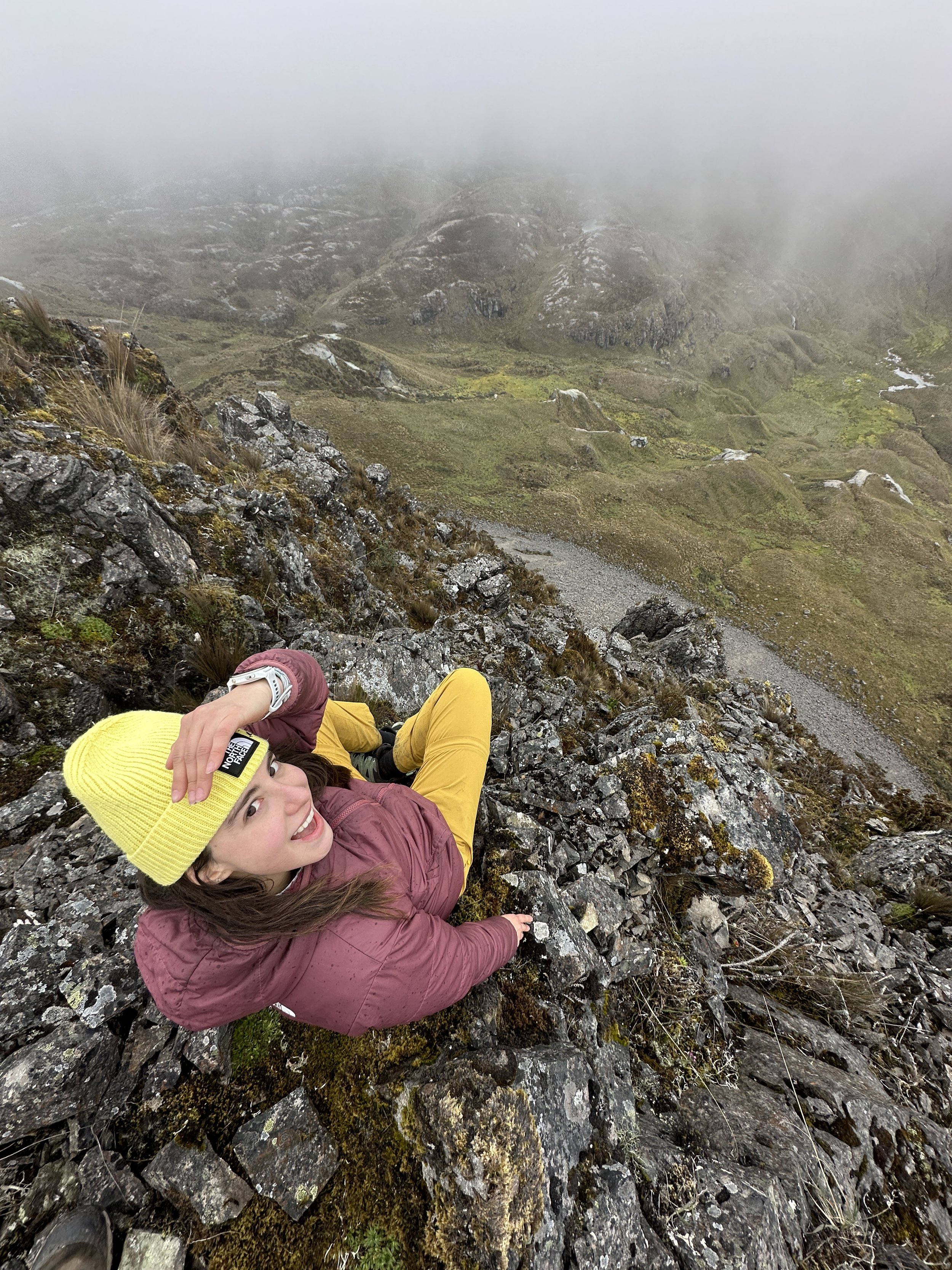 Mujer sonriendo en una cima rocosa en un paisaje montañoso con niebla