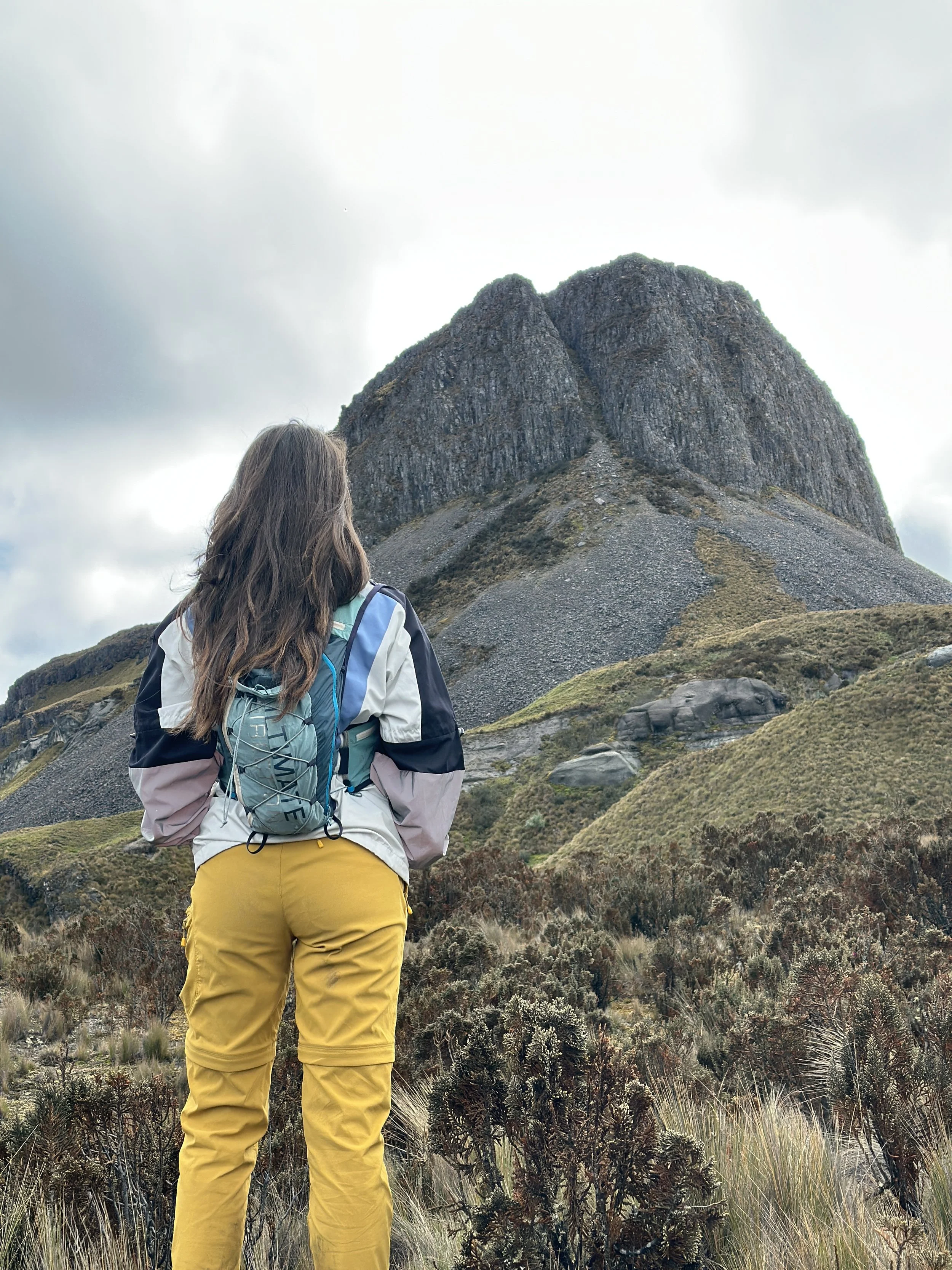 Una mujer con mochila observa una formación rocosa en un paisaje montañoso.