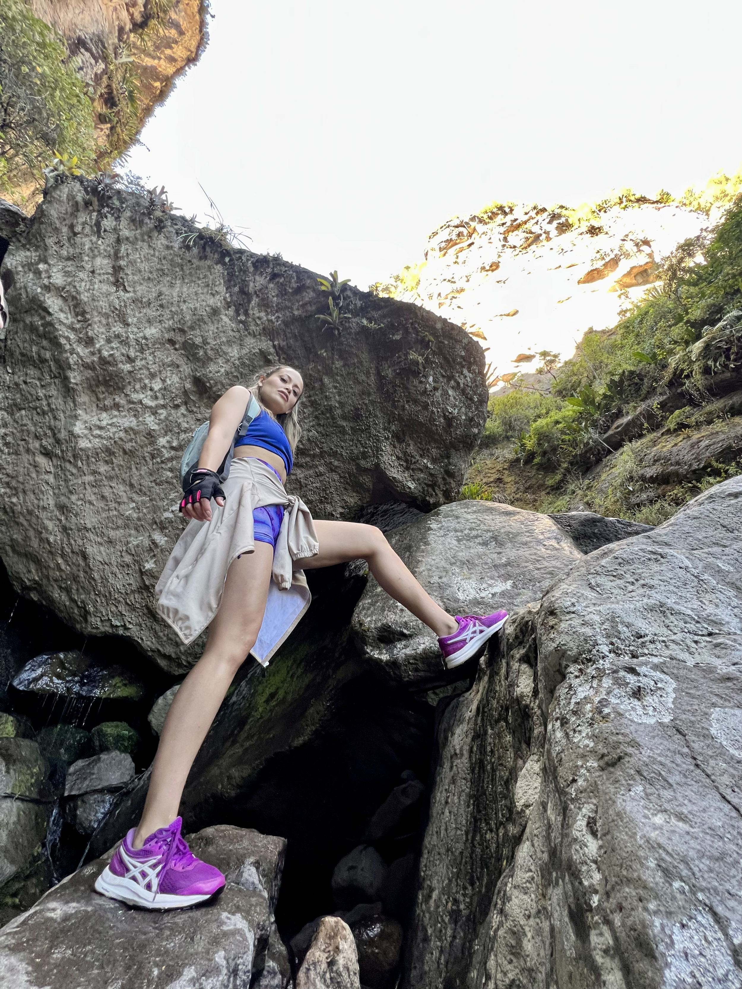 Una mujer haciendo escalada en rocas en un entorno natural con vegetación y montaña al fondo.