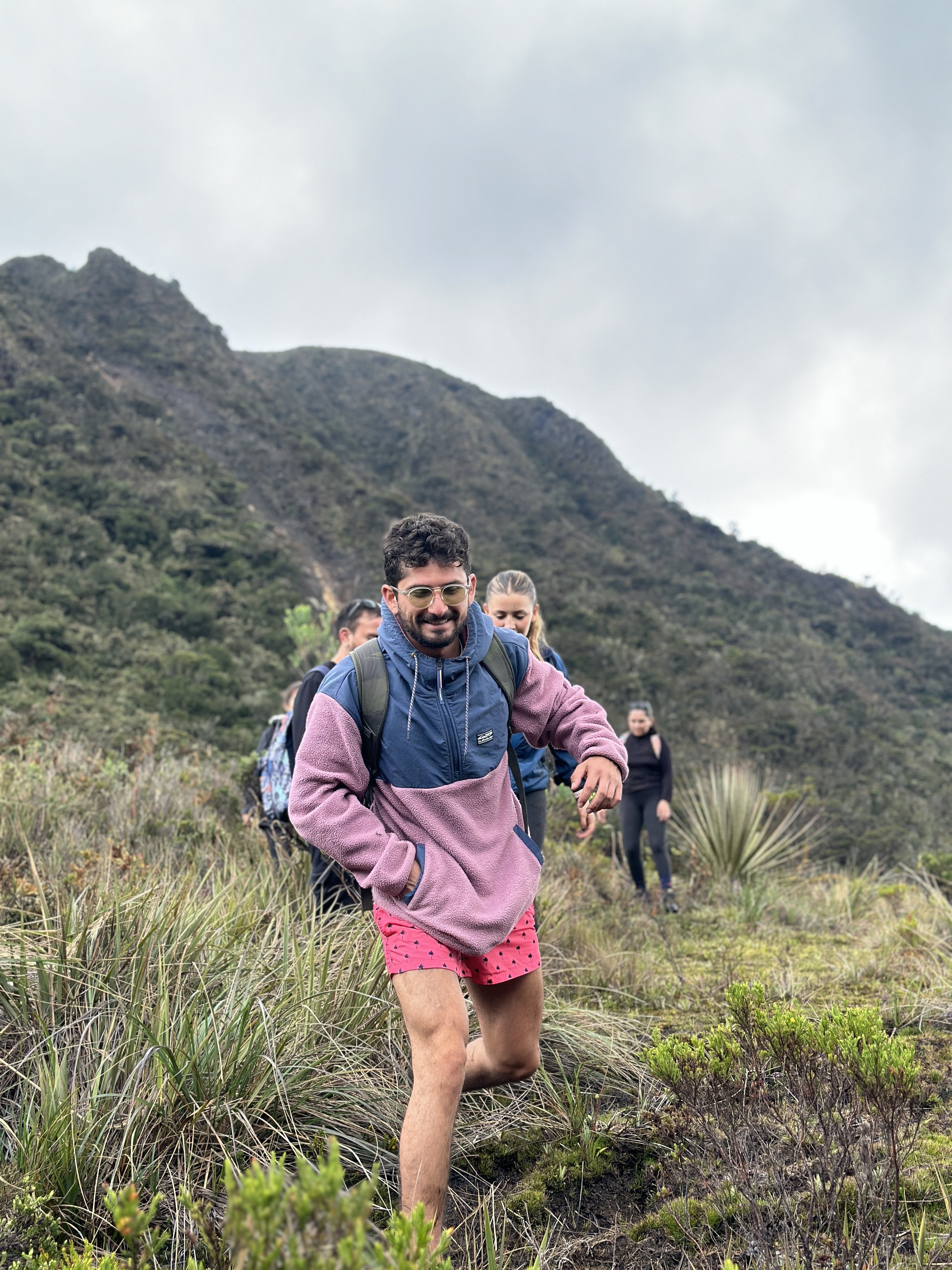 Grupo de personas caminando en una caminata por un paisaje natural montañoso. La persona en primer plano lleva gafas, sudadera y pantalones cortos rosas con puntos