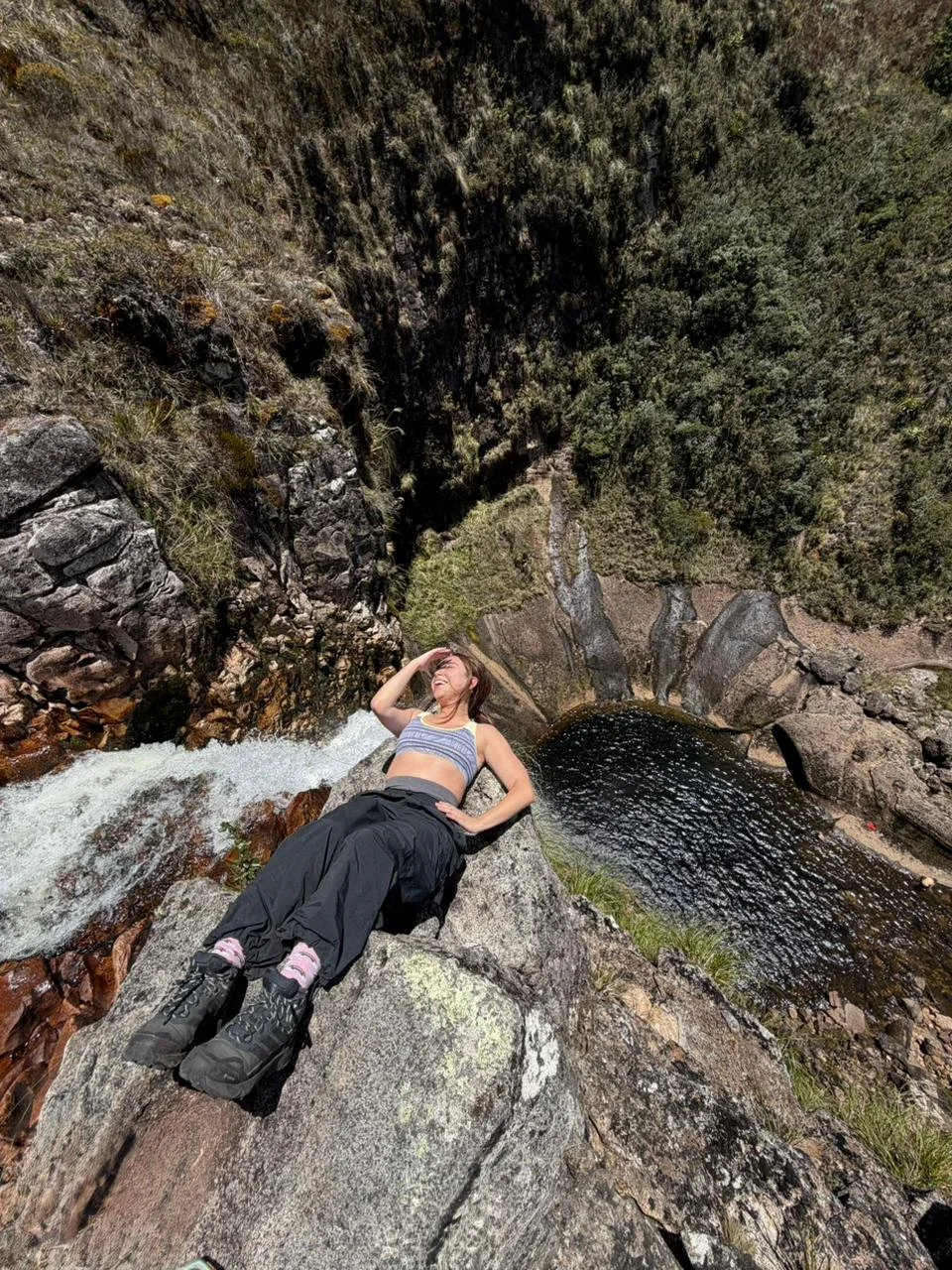 Mujer descansando en una roca cerca de un río en un cañón, rodeada de vegetación y rocas.