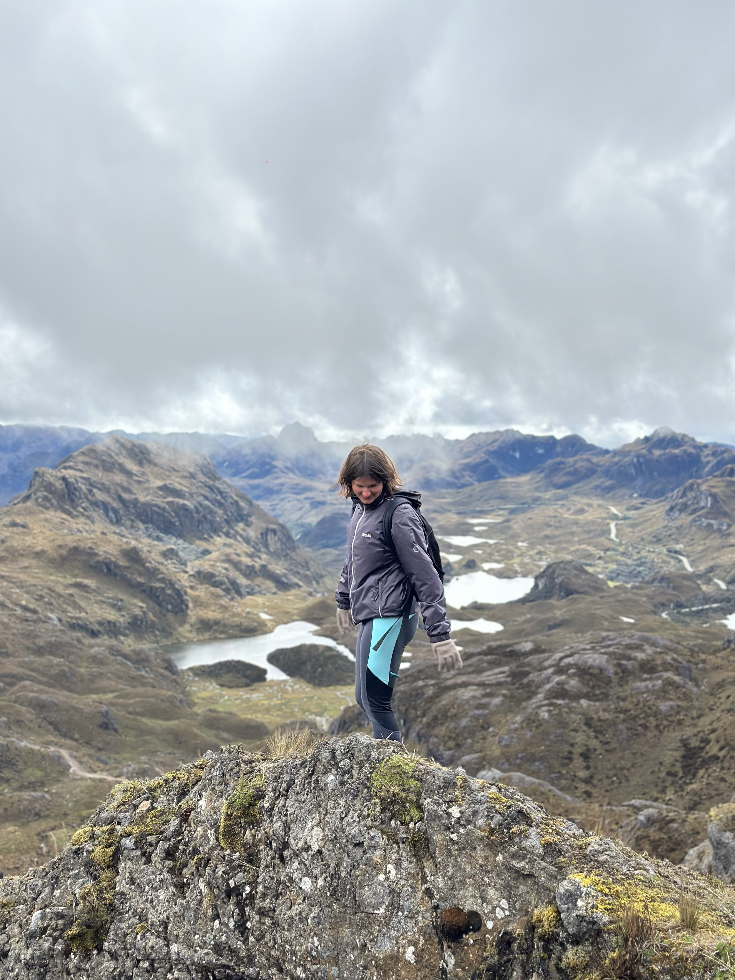 Persona caminando en paisaje montañoso con lagos y nubes en el cielo.