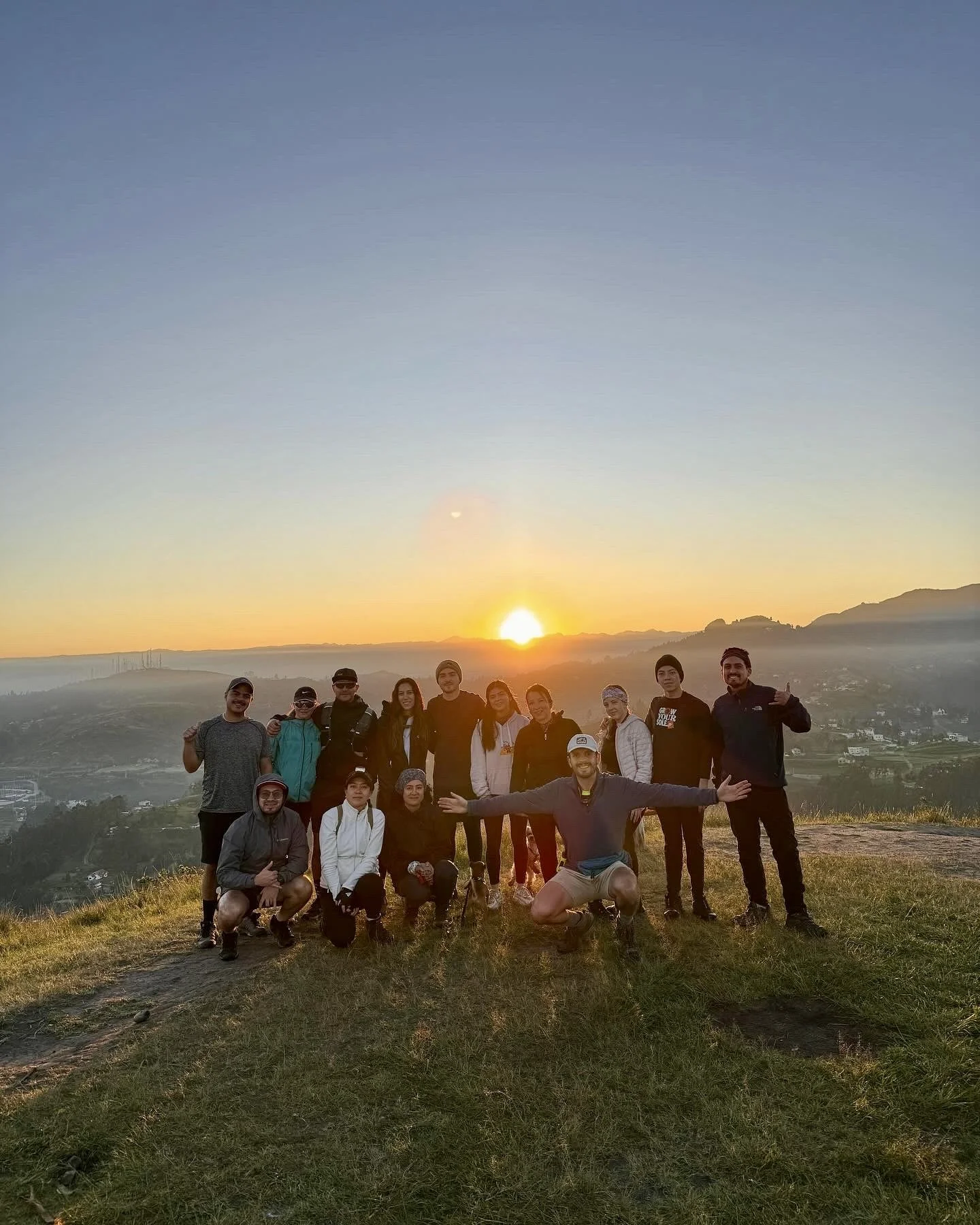 Grupo de personas en un evento al aire libre durante el amanecer en una colina con vista a un valle.