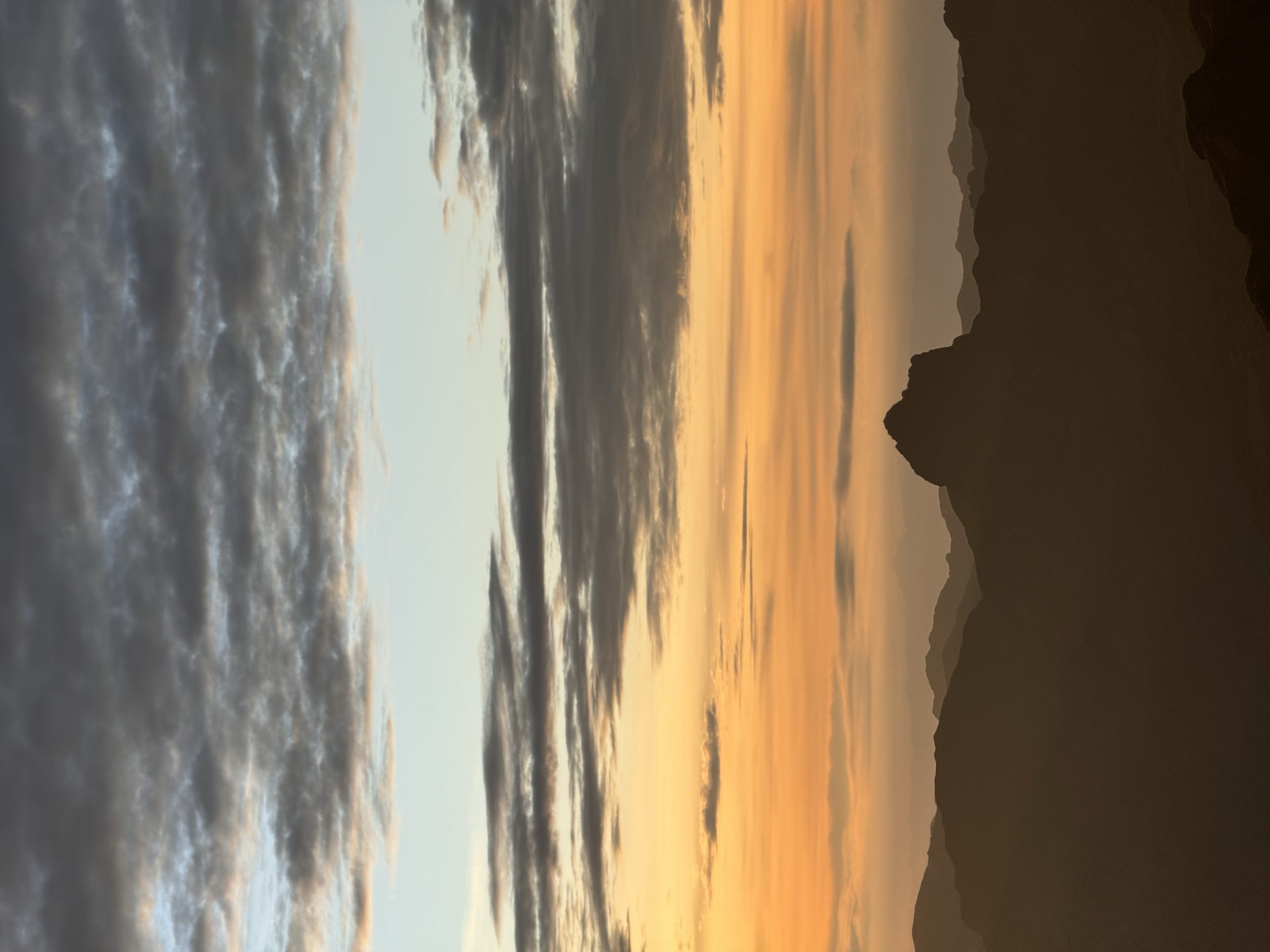 Atardecer con cielo nublado sobre una cadena montañosa con siluetas oscuras.