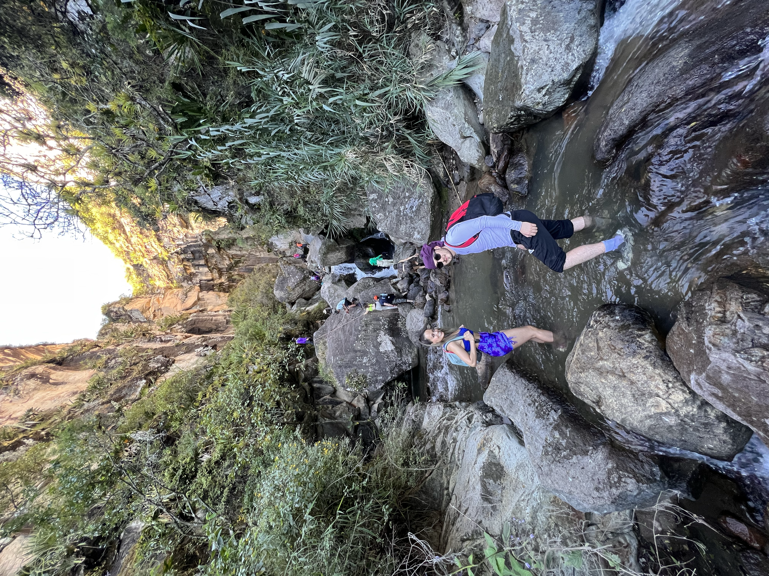 Personas explorando un río en un área natural con rocas y vegetación exuberante.