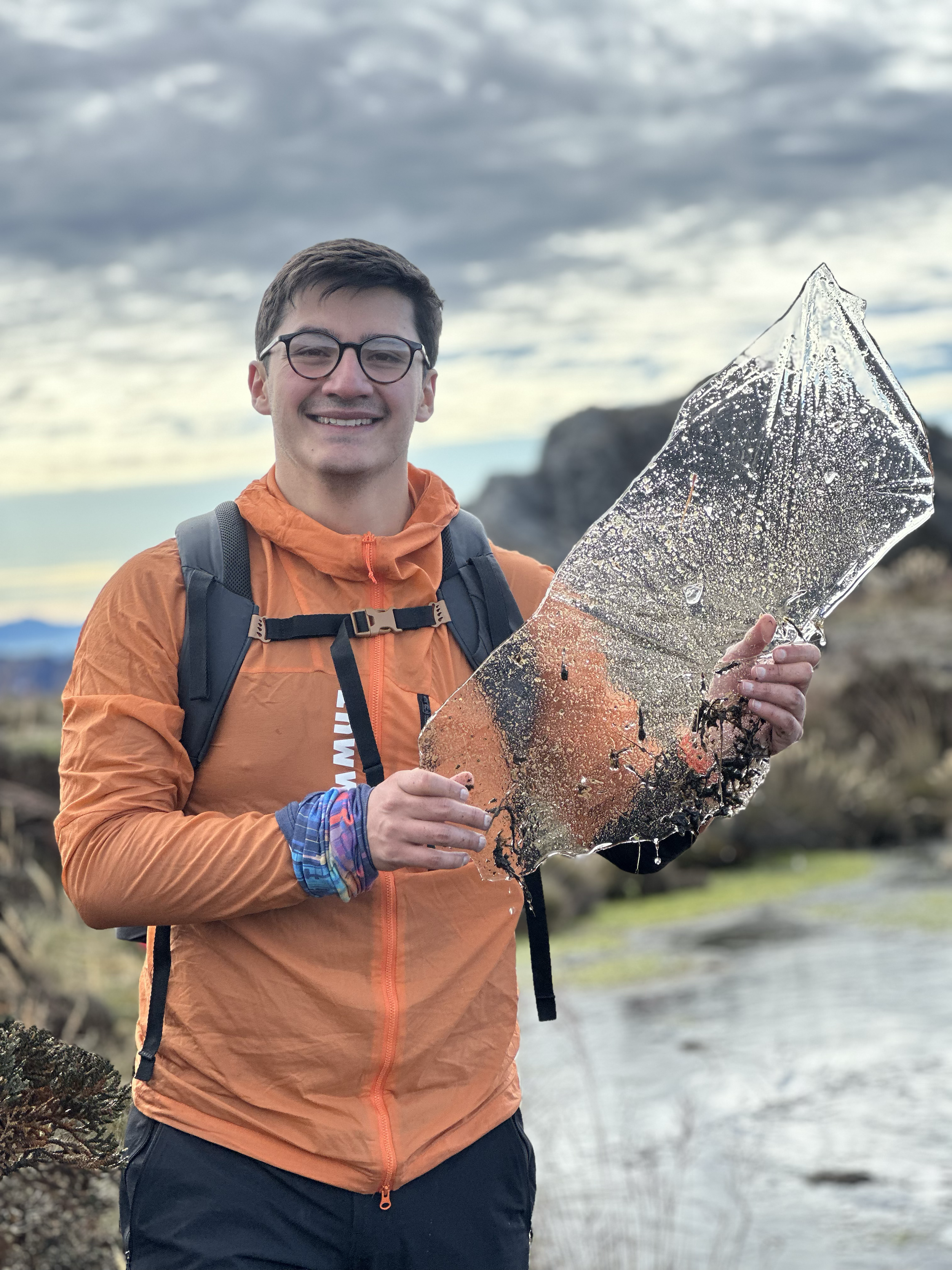 Joven montañista sosteniendo un trozo de hielo en un paisaje natural con cielo nublado.
