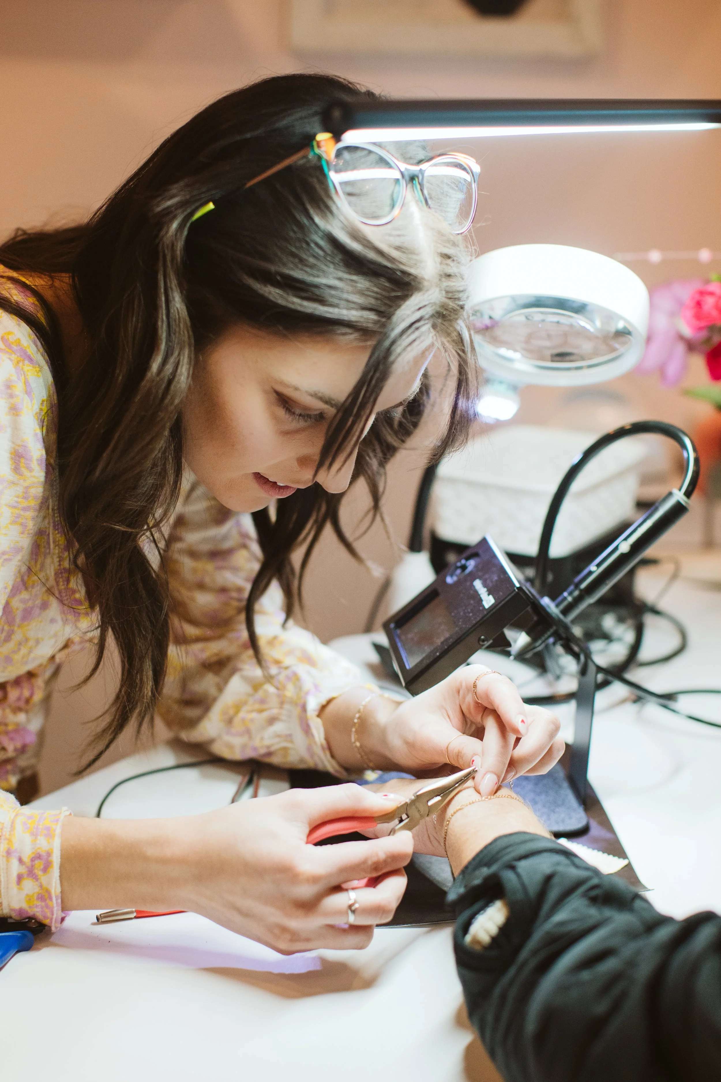 A woman getting her nails done by a nail technician at a salon, with a bright light and magnifying lamp illuminating the workspace.