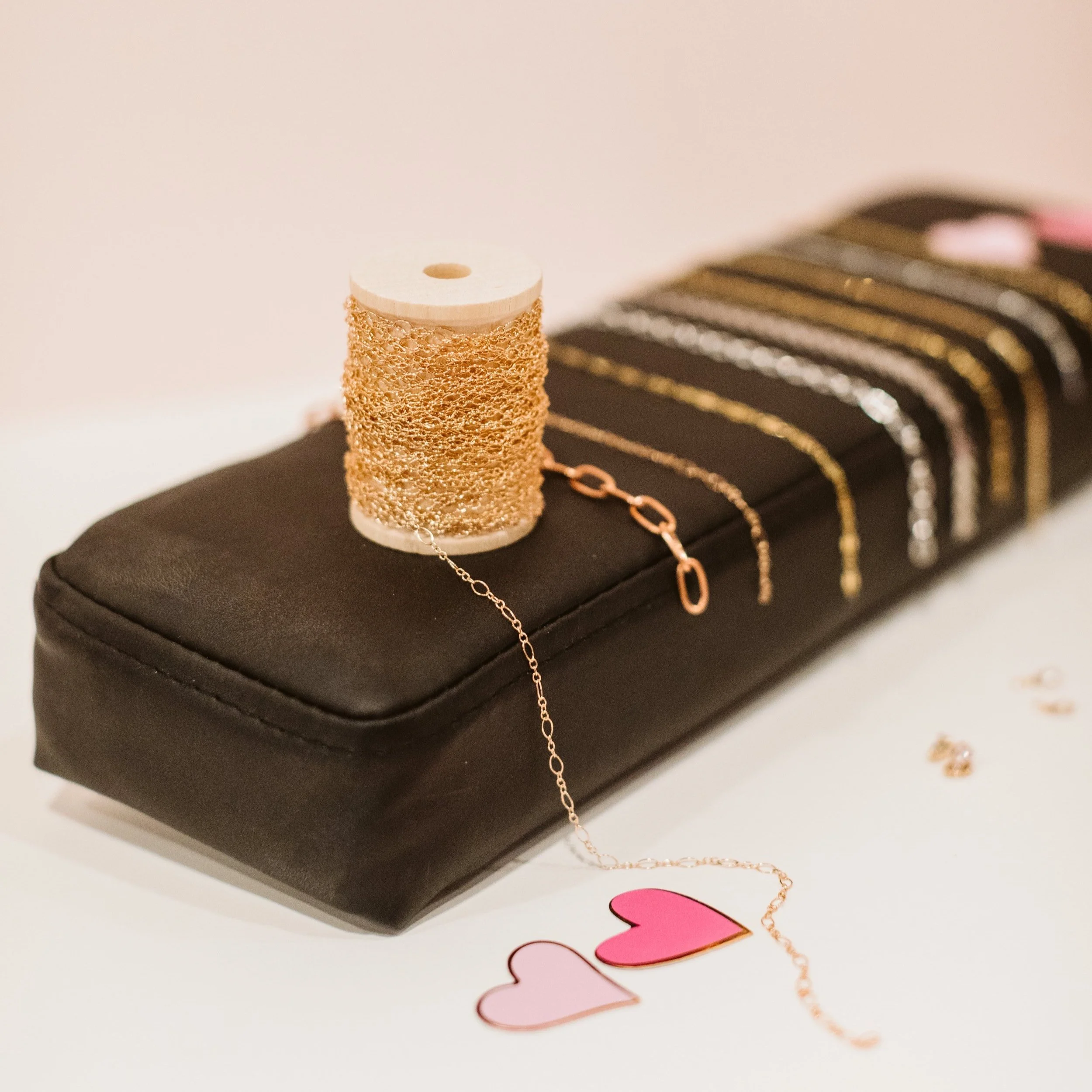 Gold jewelry, including a chain and bracelets, displayed on a black case with heart-shaped paper cutouts nearby.
