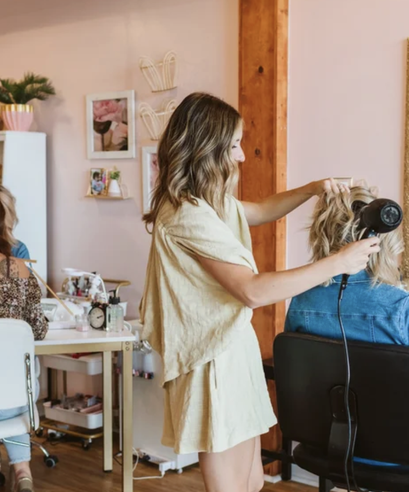 A woman receiving a manicure at a salon, with her hands being painted by a technician.