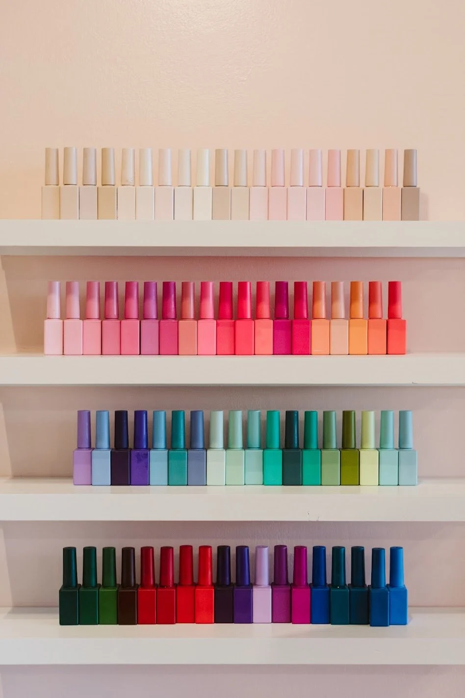 Two women in a cozy indoor setting, one smiling at the other, with shelves and a mirror in the background. Plants and beauty products are visible on the shelves.