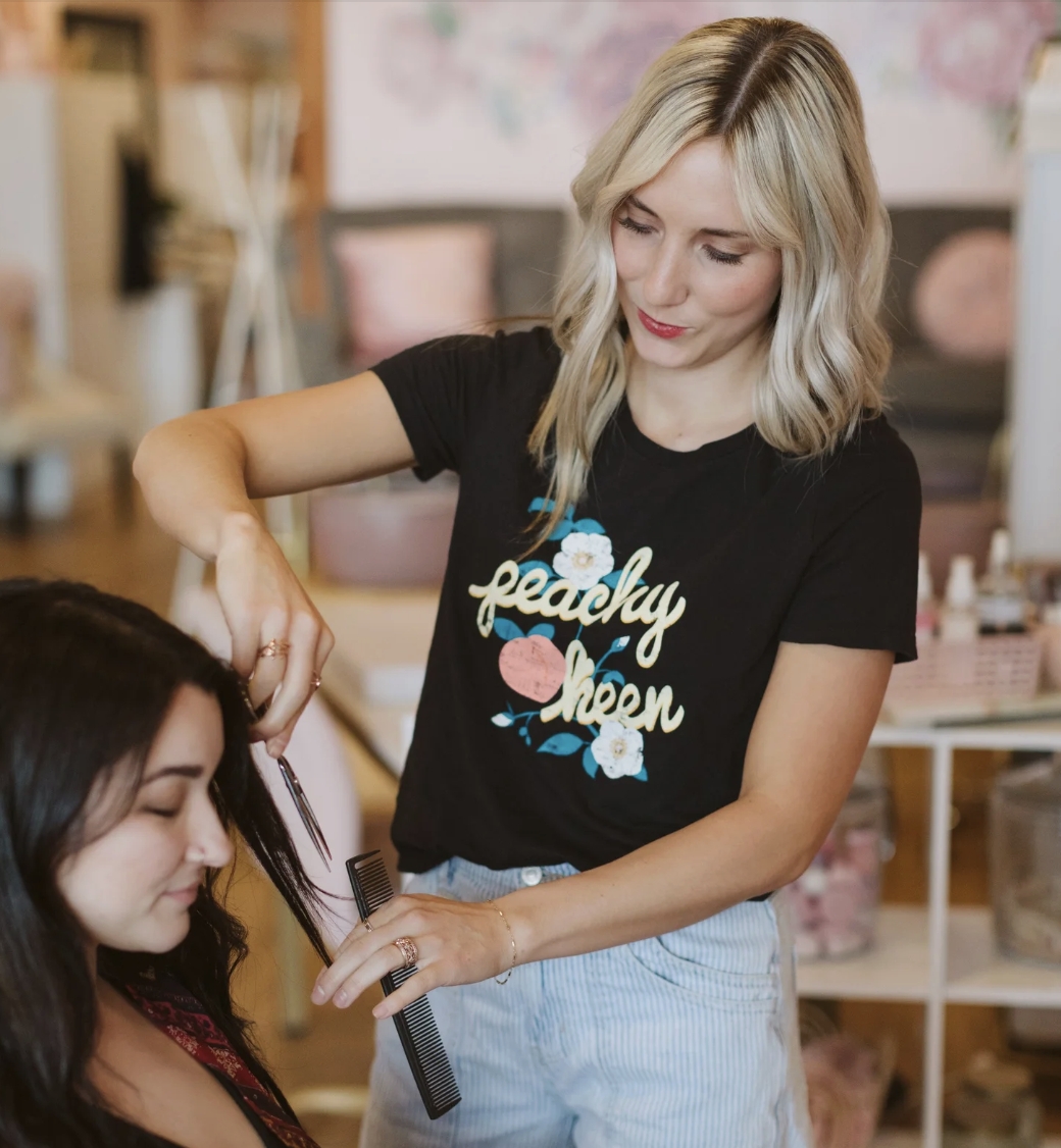 A woman with blonde wavy hair smiling at a nail technician while getting a manicure in a salon.