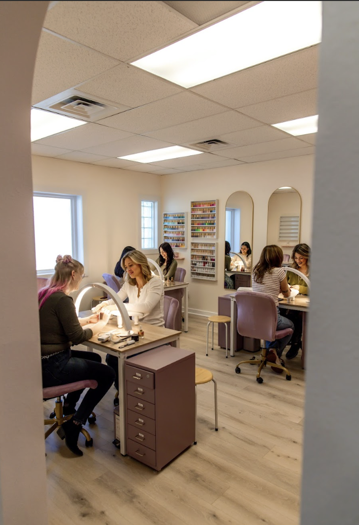 A nail salon with several women getting manicures, seated at manicure stations with nail polish displays on the walls.