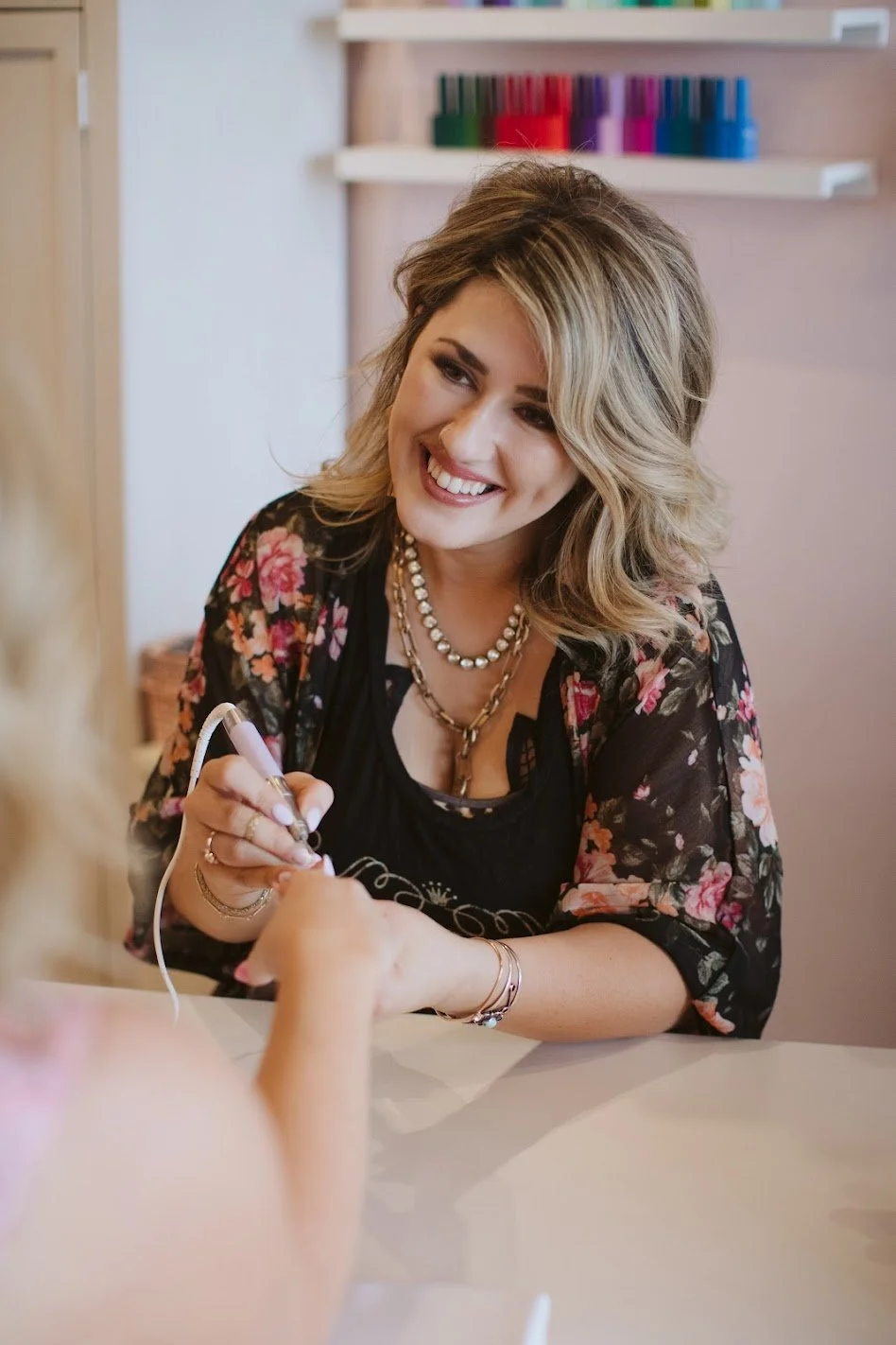 Woman cutting hair in a salon, smiling and holding scissors, wearing a white top and black pants.