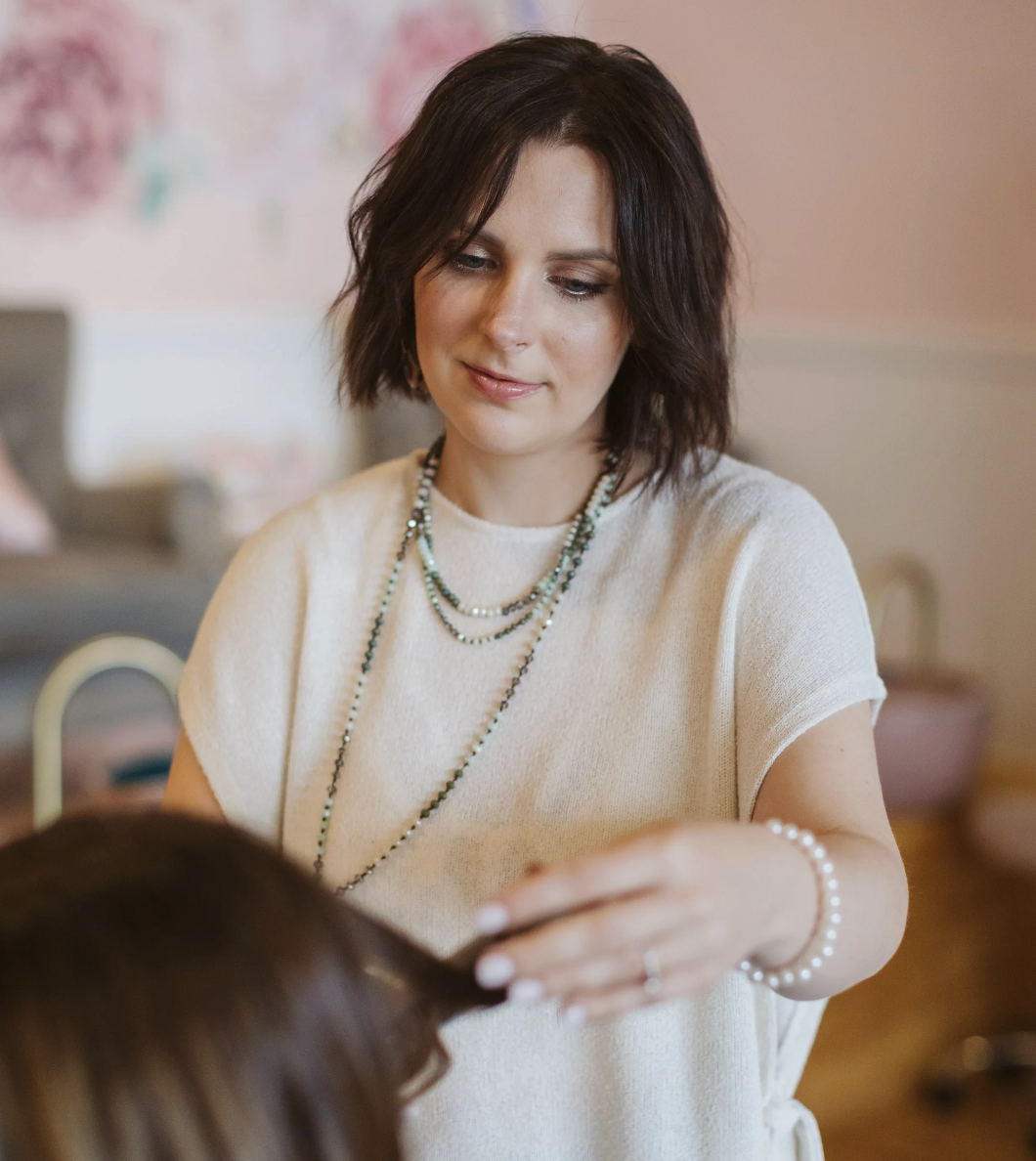 A woman with blonde wavy hair smiling at a nail technician while getting a manicure in a salon.