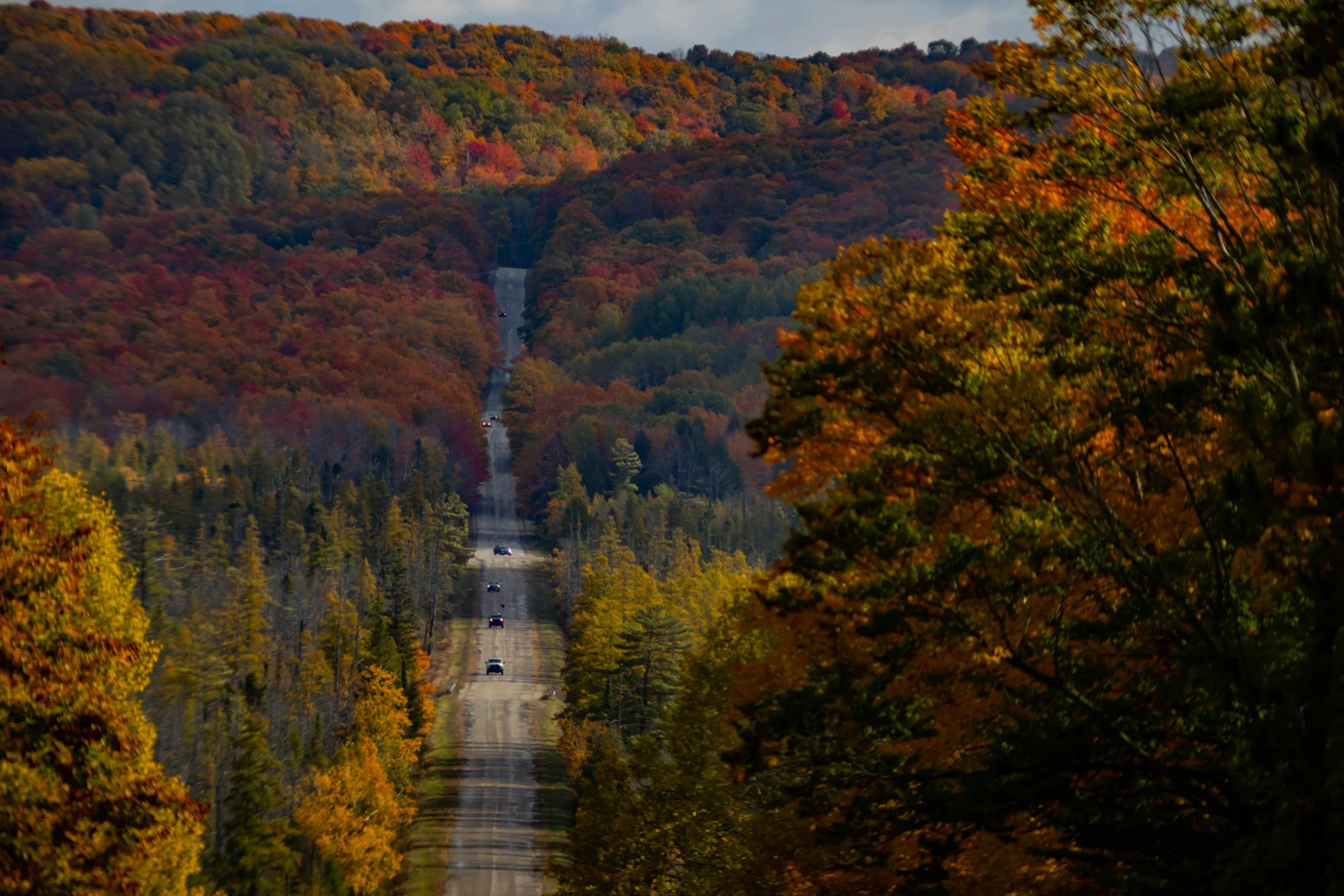 Scenic road winding through colorful red, orange, and golden autumn forests in Michigan’s Upper Peninsula.