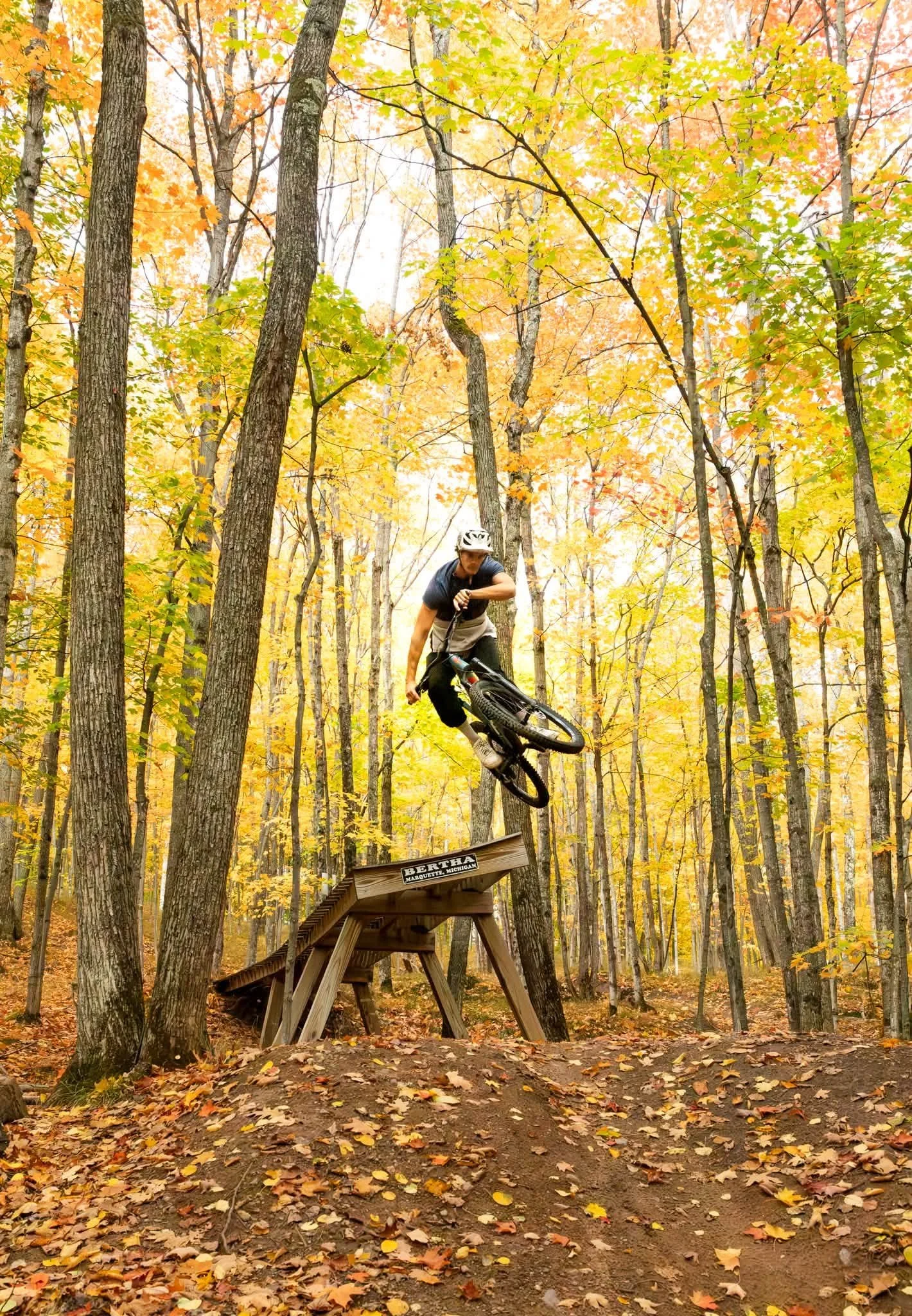Mountain biker riding a wooden trail feature through a golden autumn forest in Michigan’s Upper Peninsula.