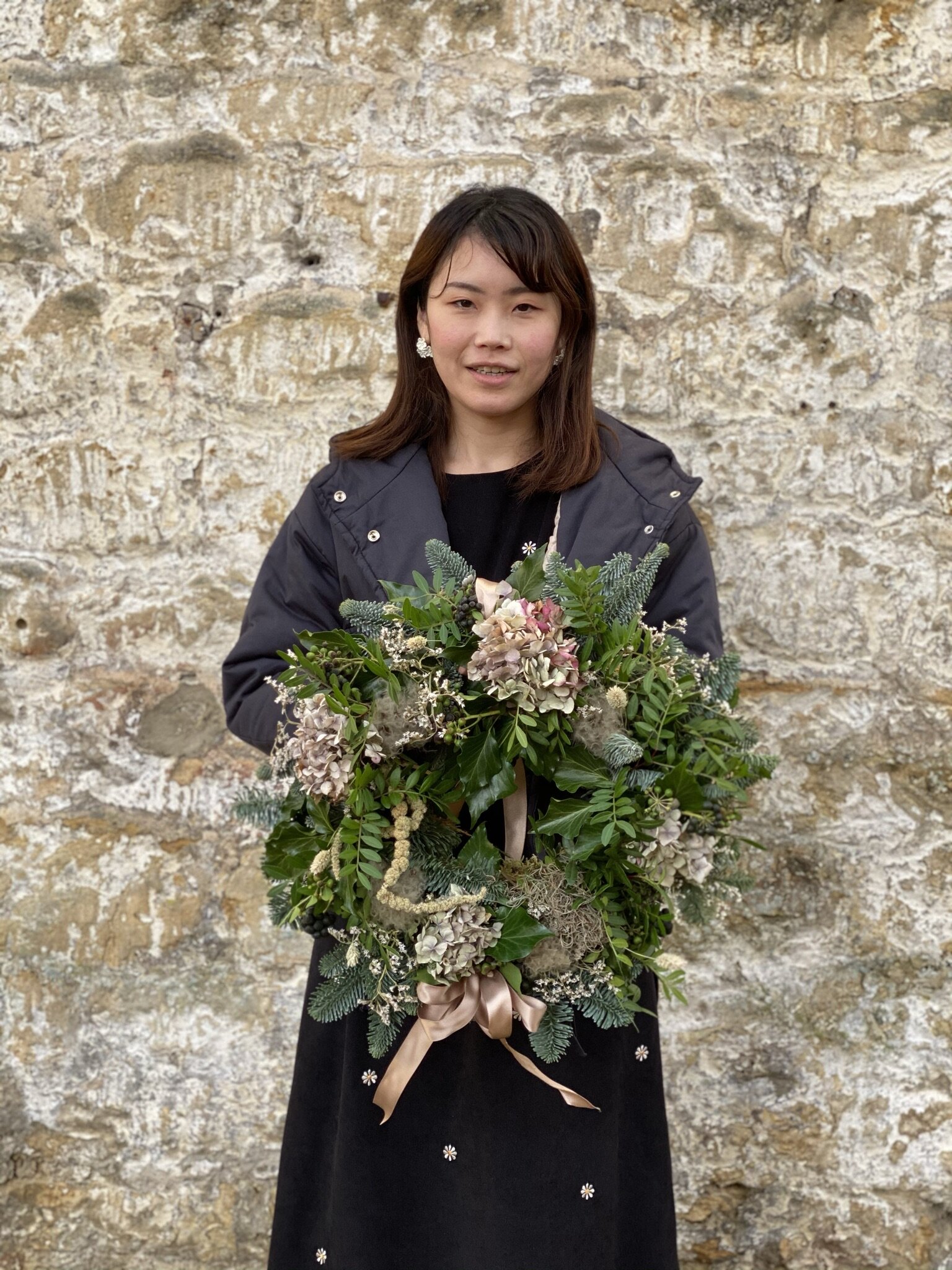 Hedgerow inspired Christmas wreath being held by student in front of a brick wall (Copy)