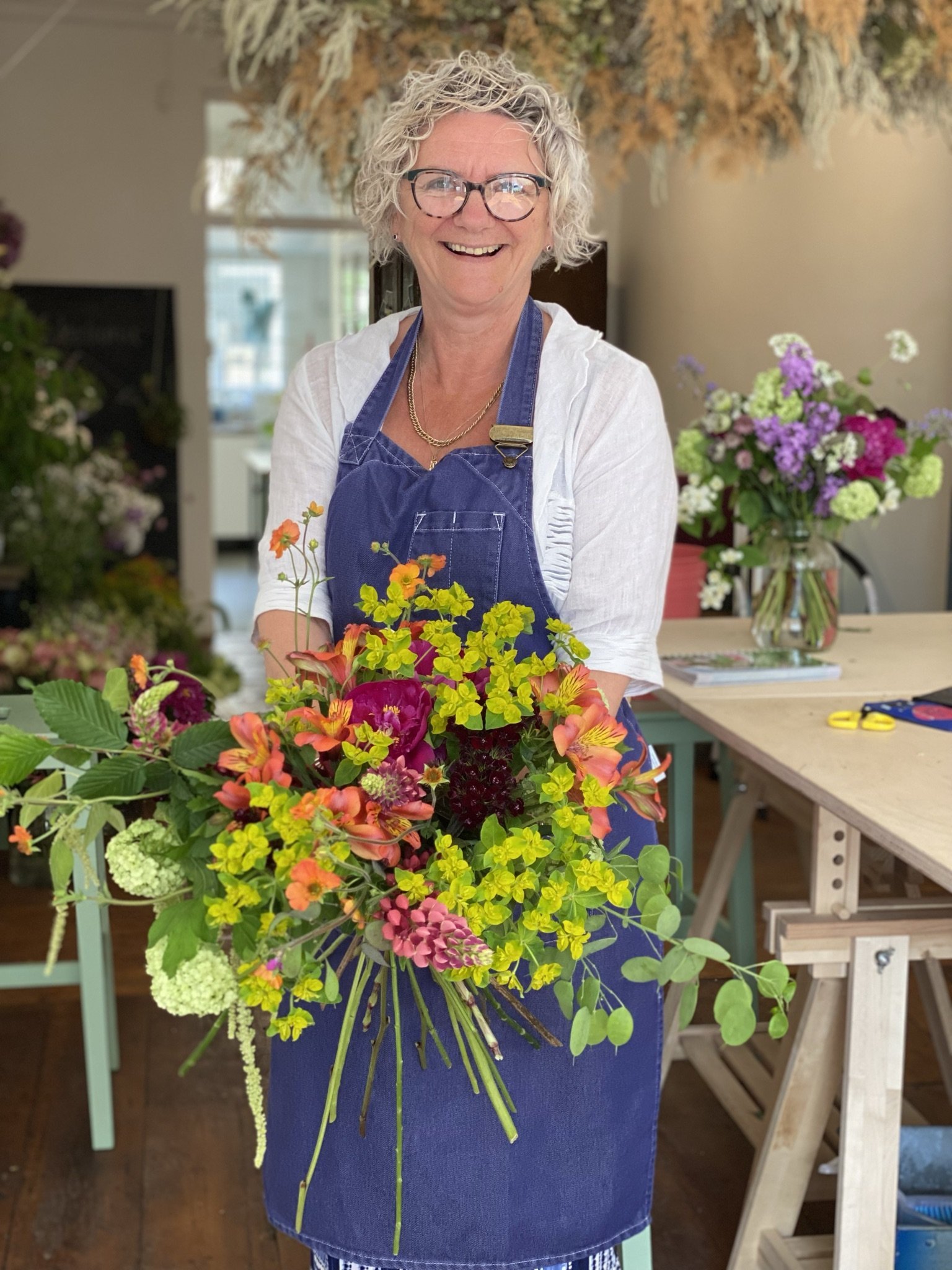 Proud, smiley student with brightly coloured flowers created on the hand tied bouquet workshop
