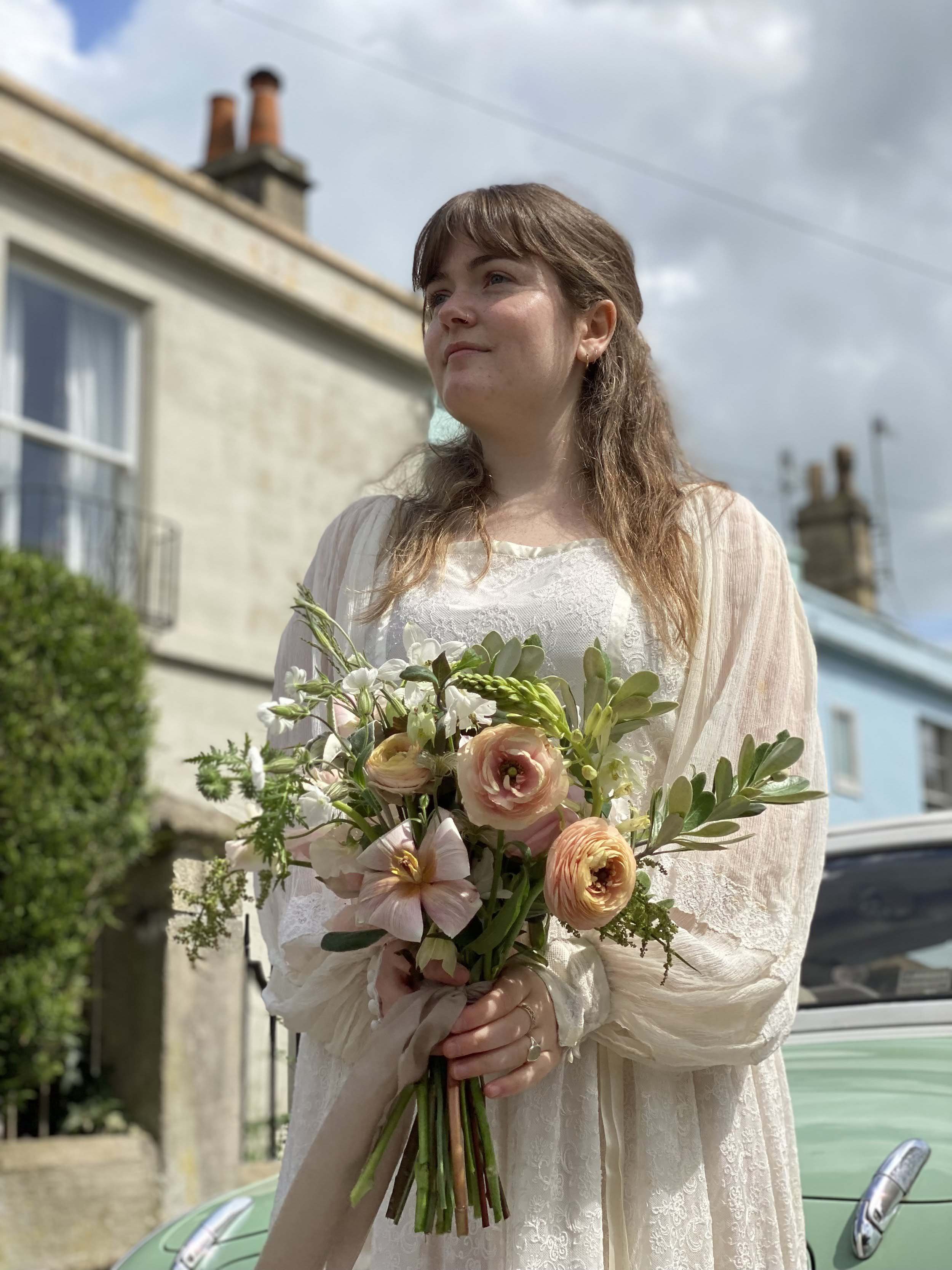 The Bath Flower School student holding her beautiful bridal bouquet in front of candy coloured houses