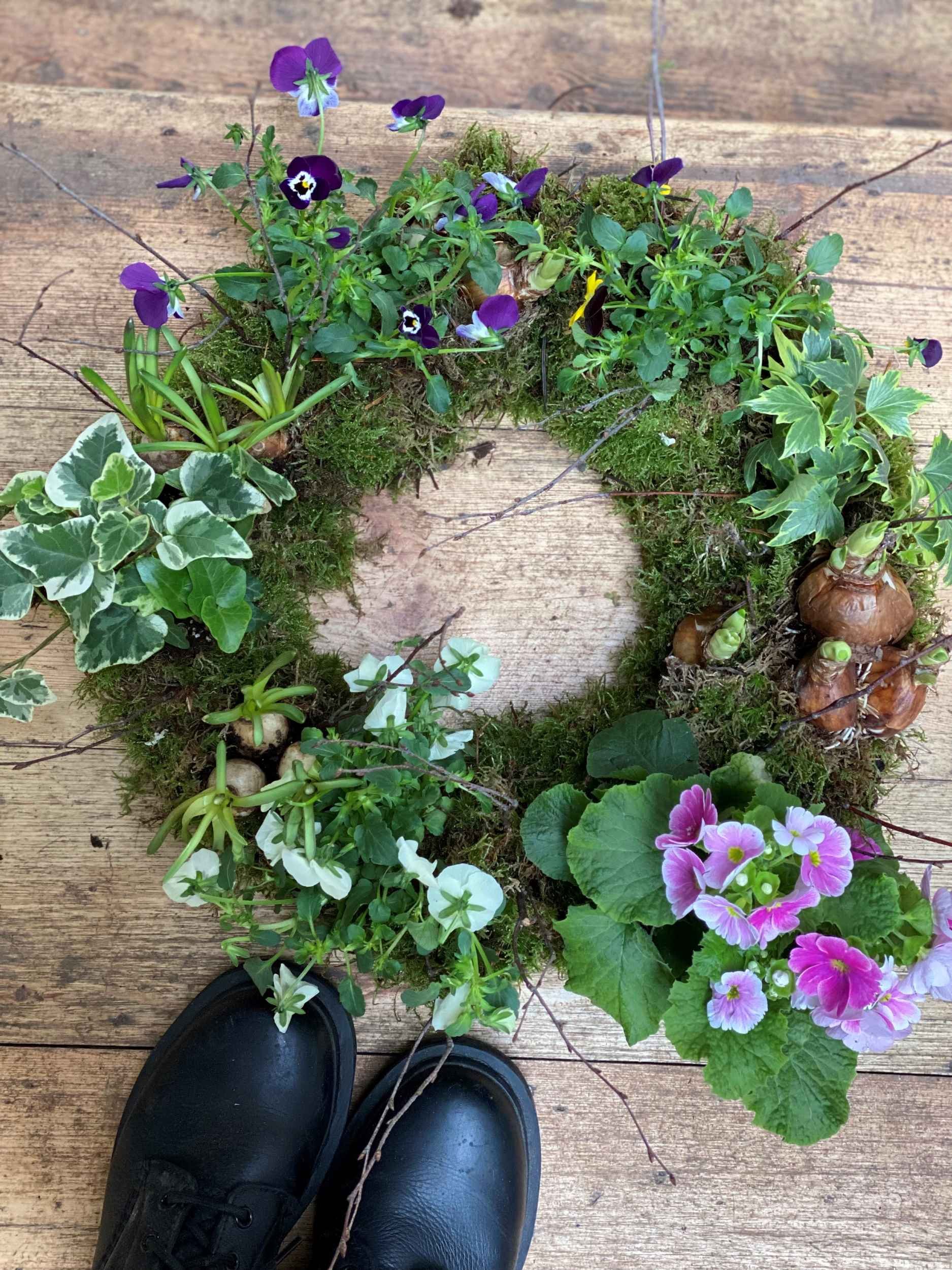 Birdseye view of a spring living wreath on floor with black boots