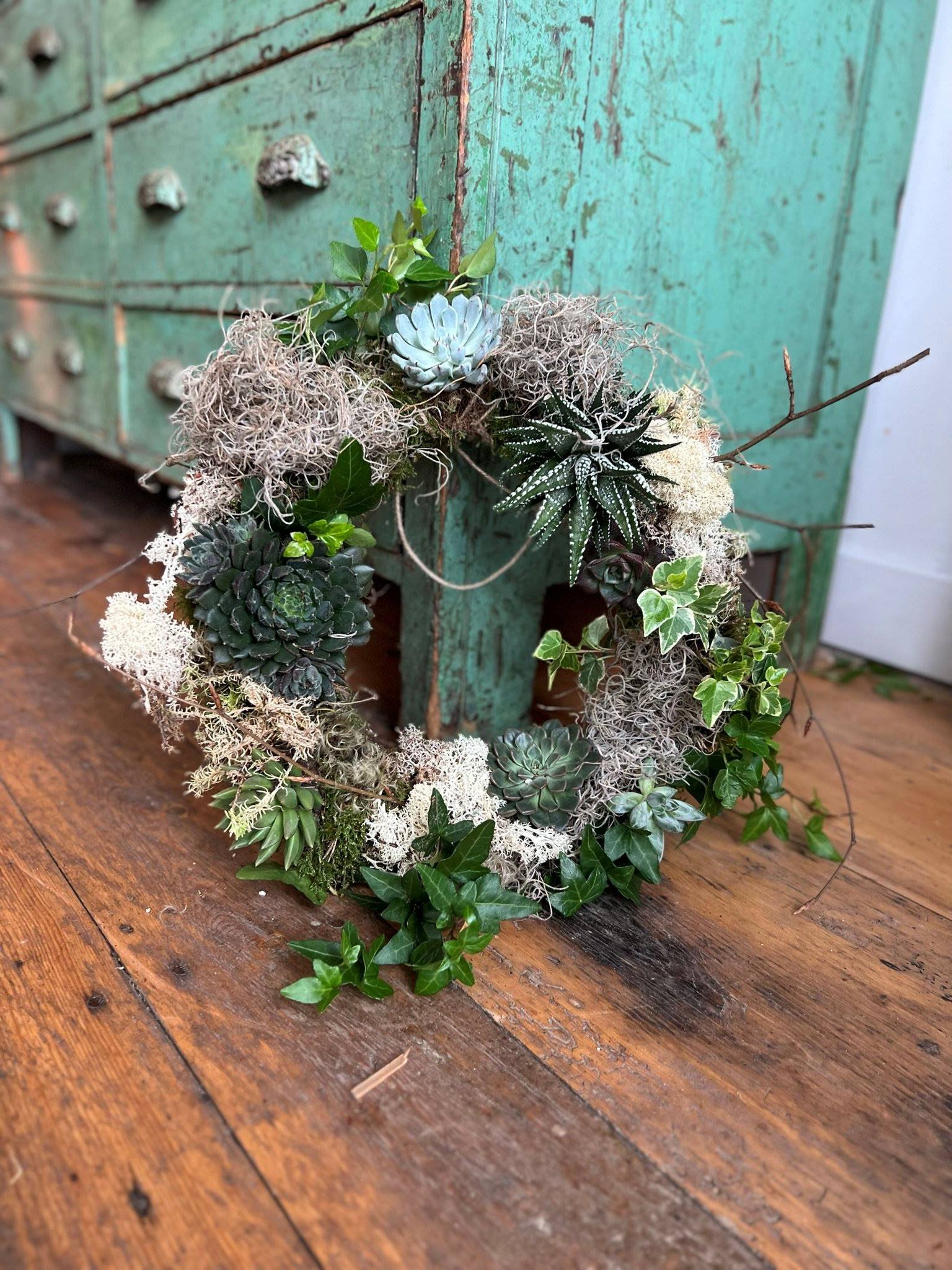 Succulent and reindeer moss living wreath against a bright green sideboard