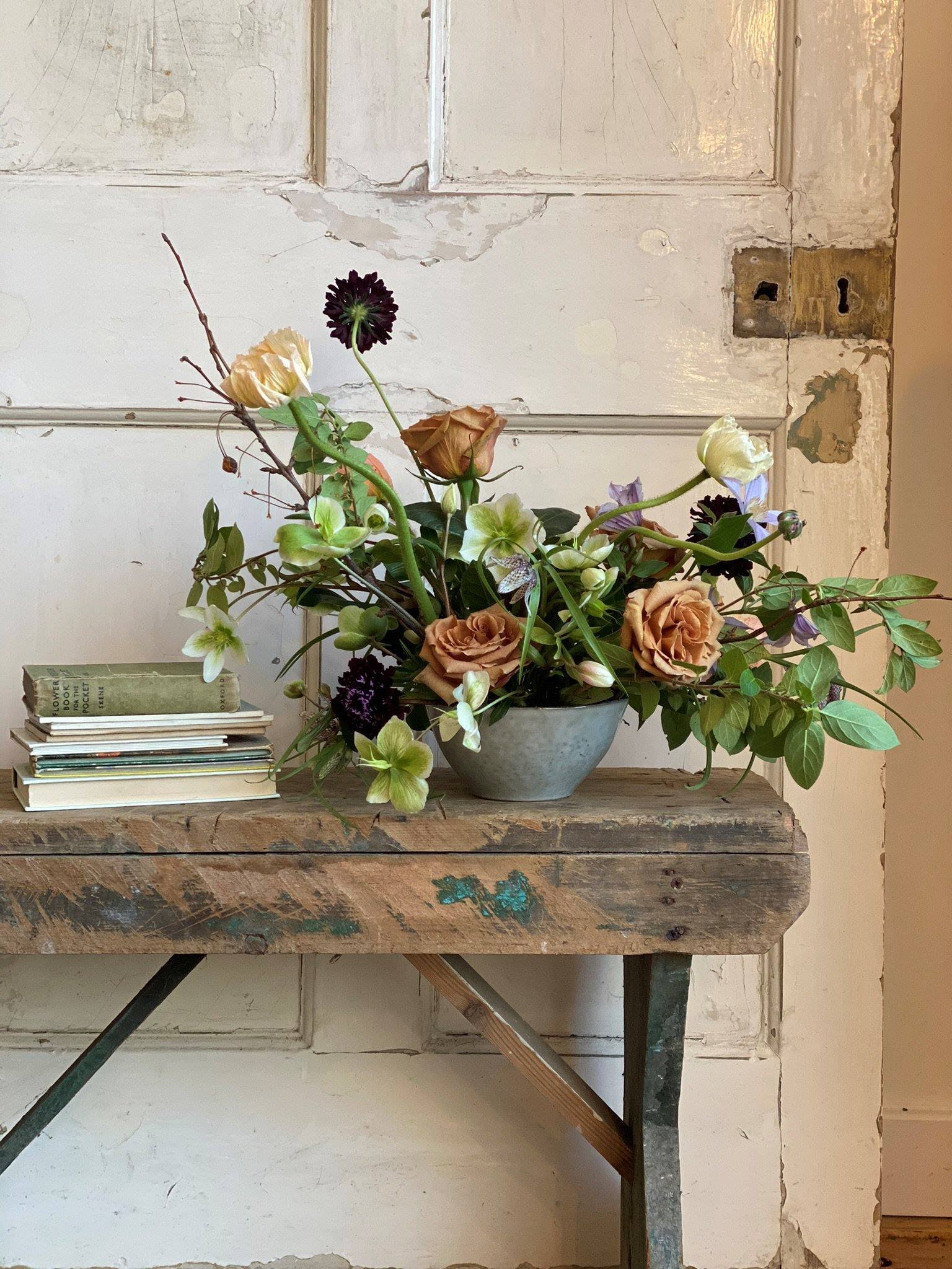 An eco-friendly floral arrangement with a bowl of flowers placed on a bench in front of a door