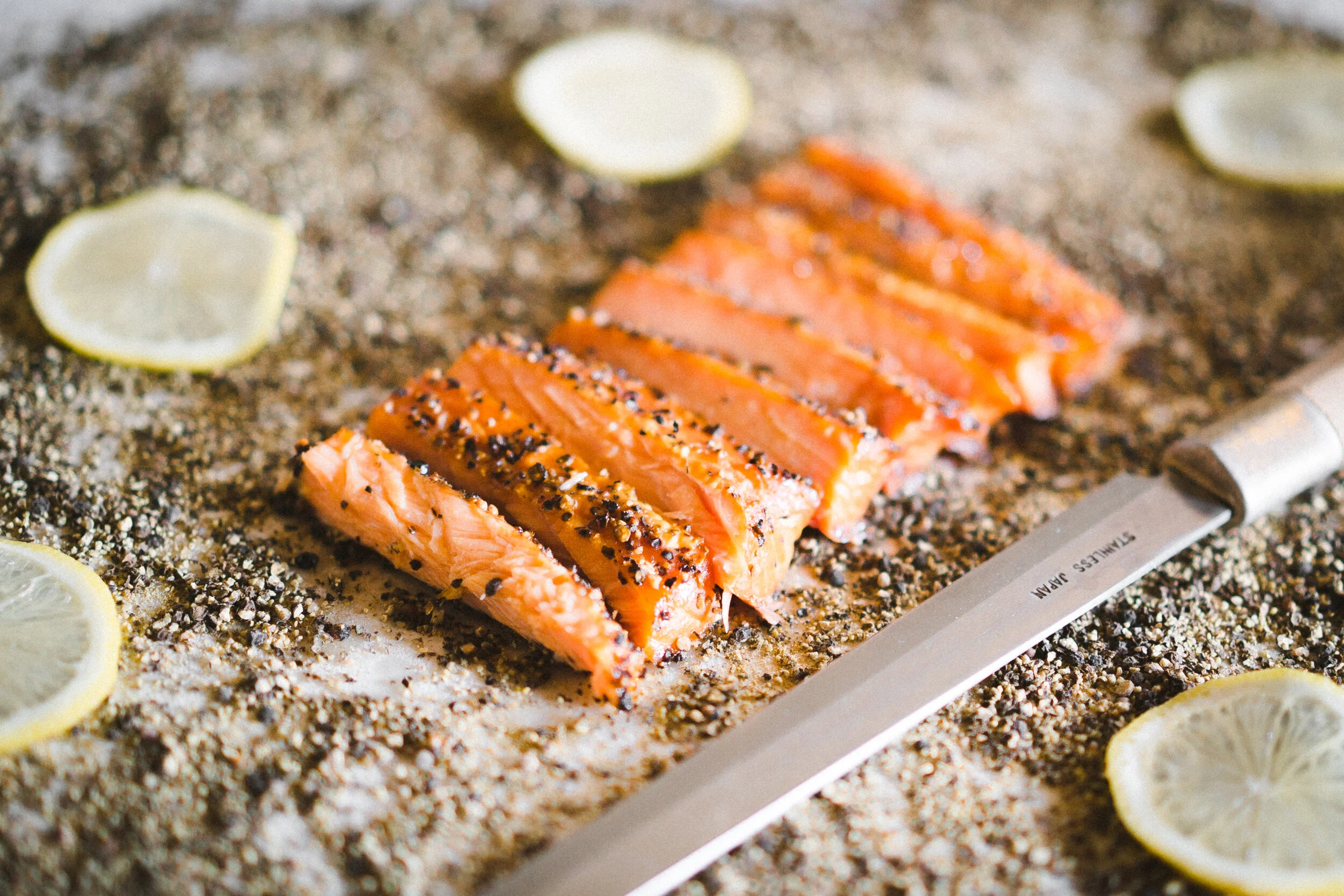 Artistic Shot of Sliced Smoked Black Pepper Salmon On Surface Dusted With Black Pepper, Surrounded by Intimidating Slices of Lemon