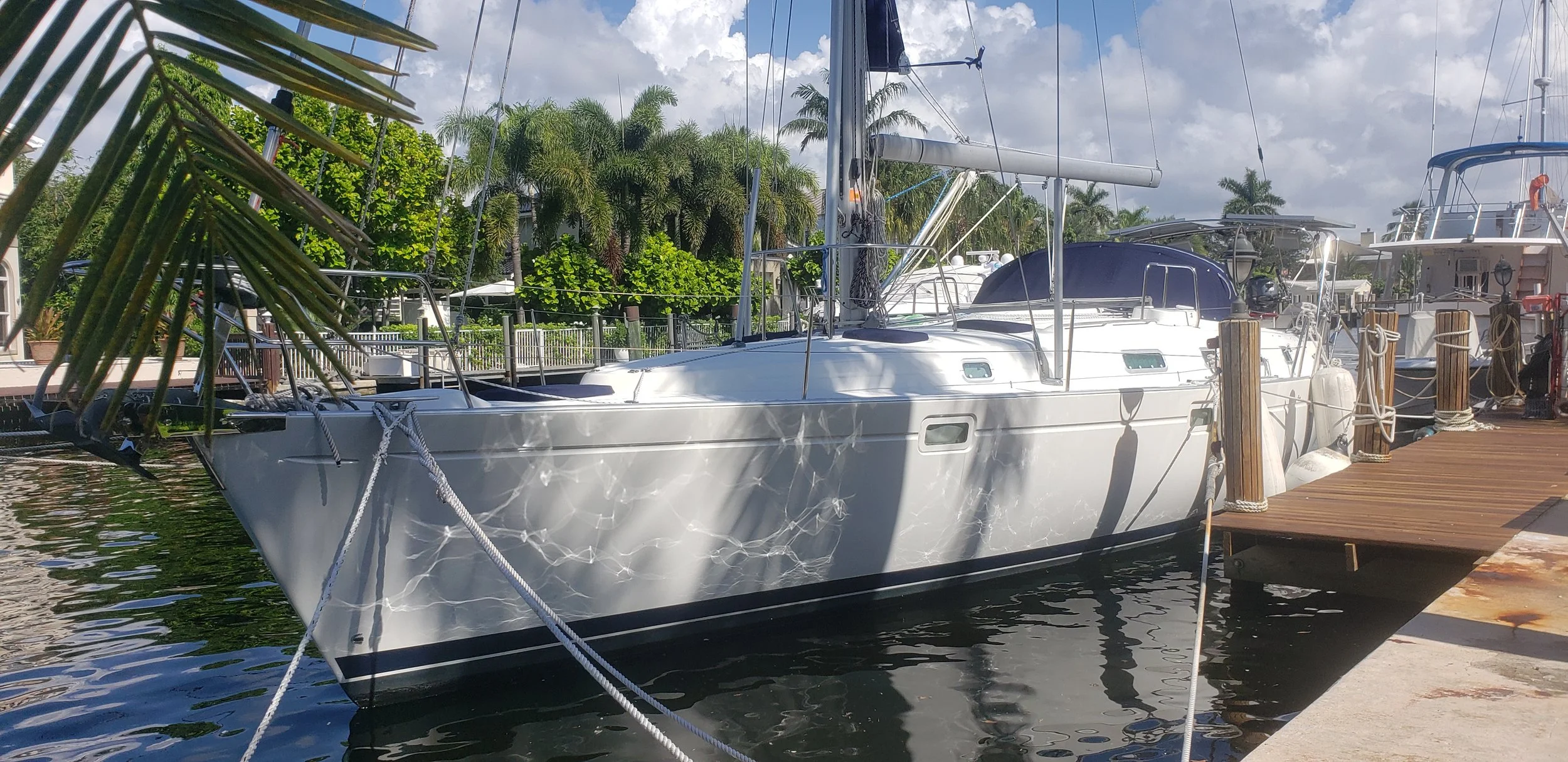 A white sailing yacht docked at a marina with palm trees and other boats in the background.