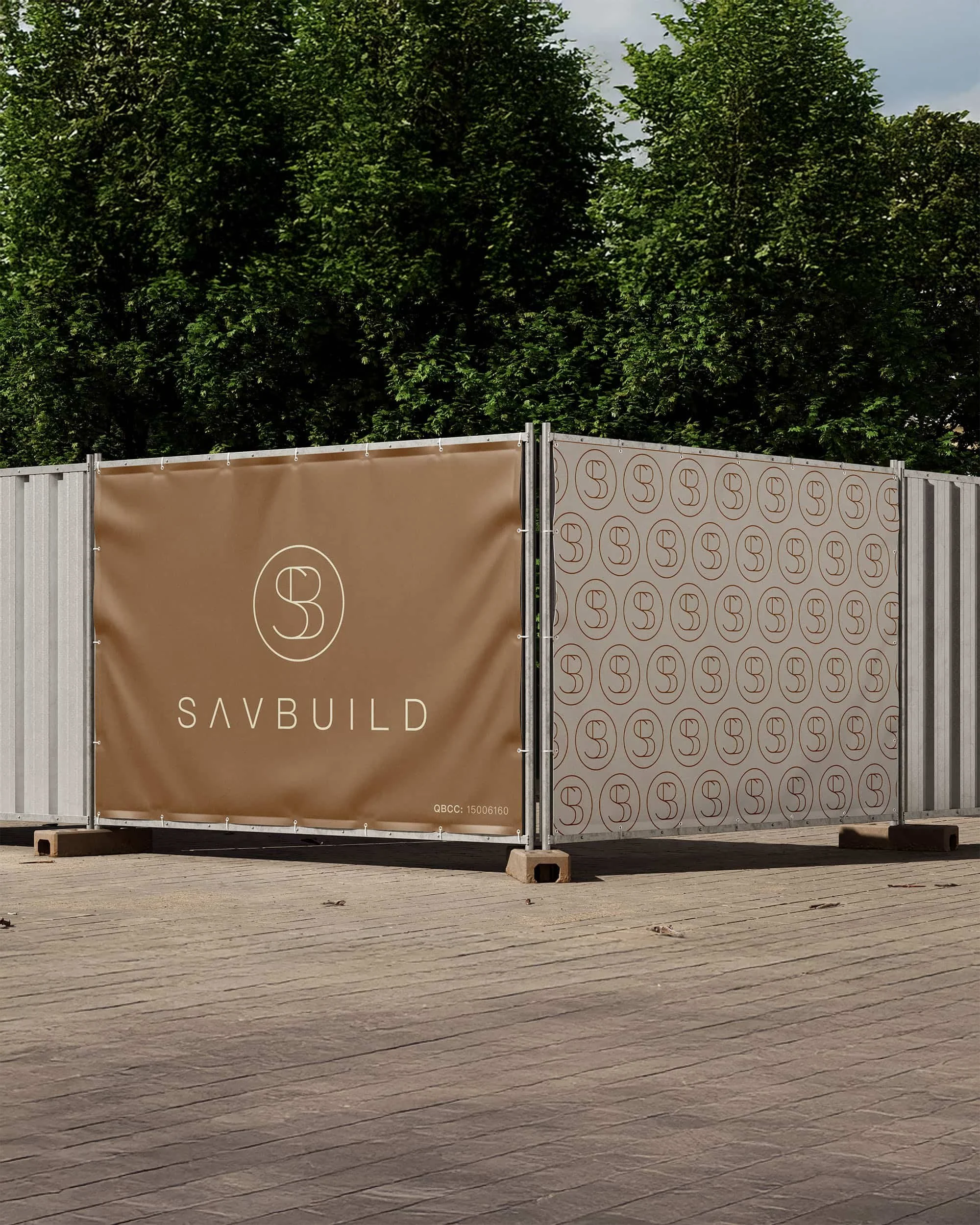 Construction site fencing with a brown panel displaying the 'SAVBUILD' logo, above a pattern of repeating logos on another panel, set against a backdrop of trees.
