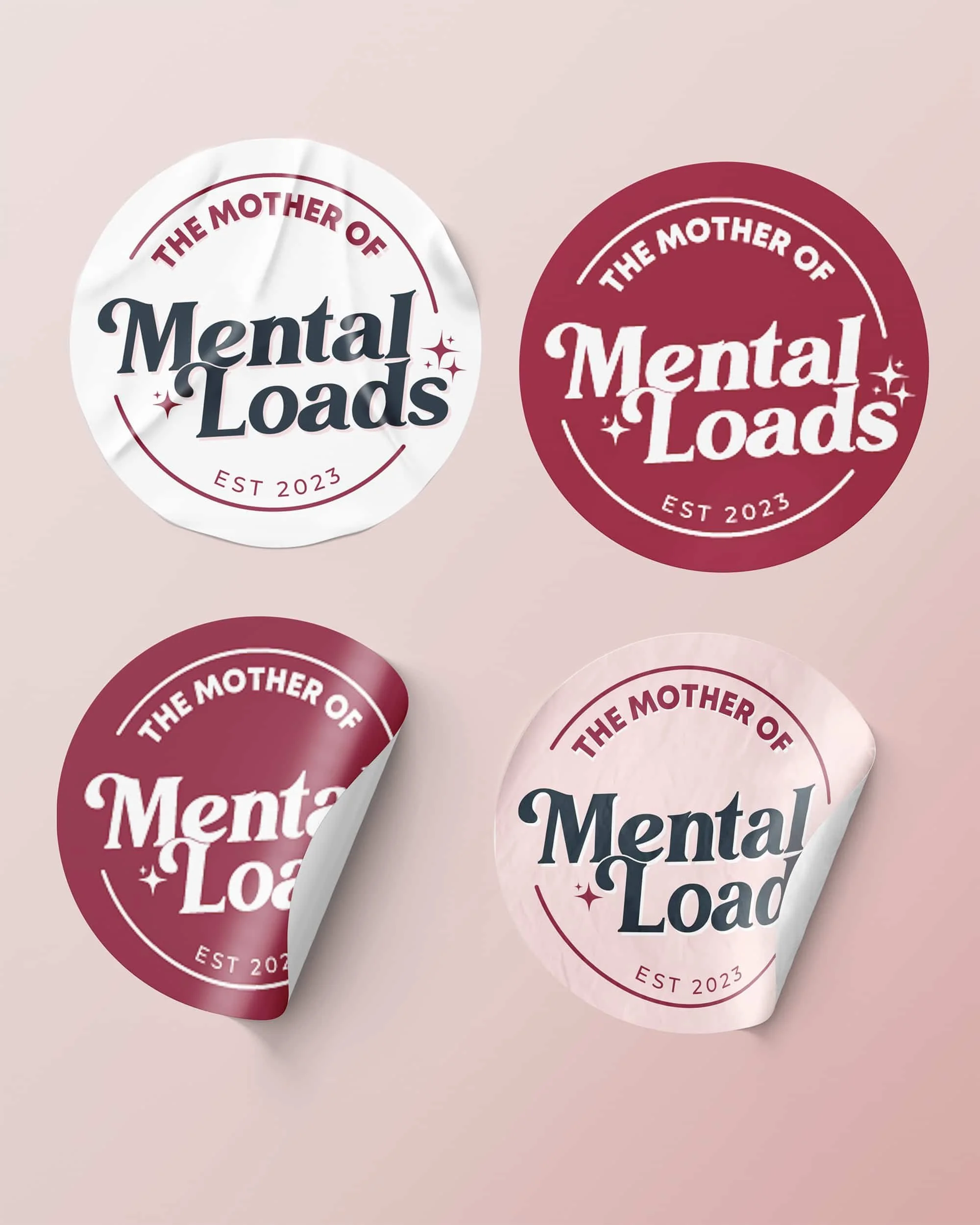 Four stickers with the text "The Mother of Mental Loads," "EST 2023," with two in a dark pinkish color and two in a light pink or white color, arranged on a light pink background.