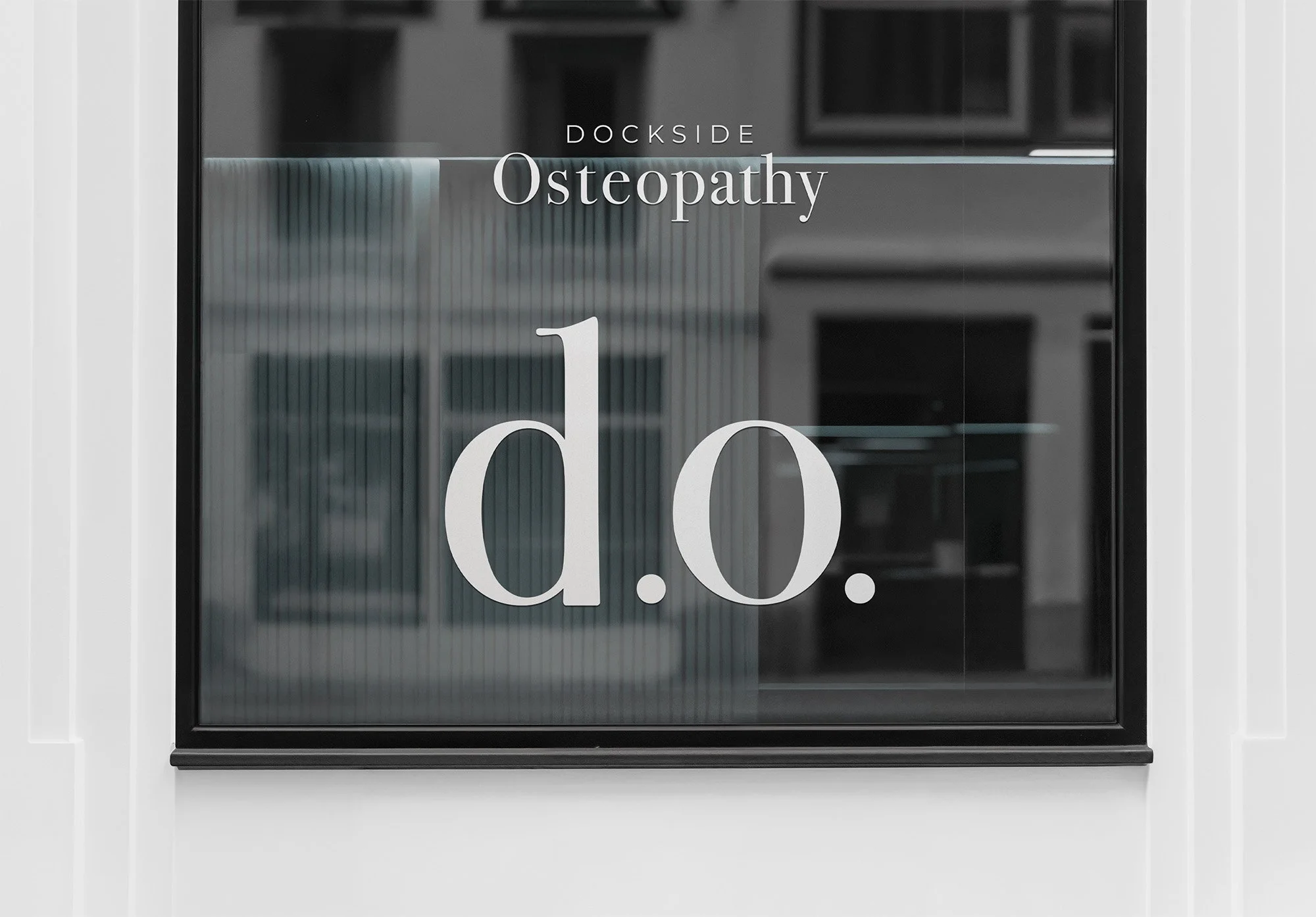 Sign reading 'Dockside Osteopathy' with large 'd.o.' letters on a window, reflecting a building in the background.