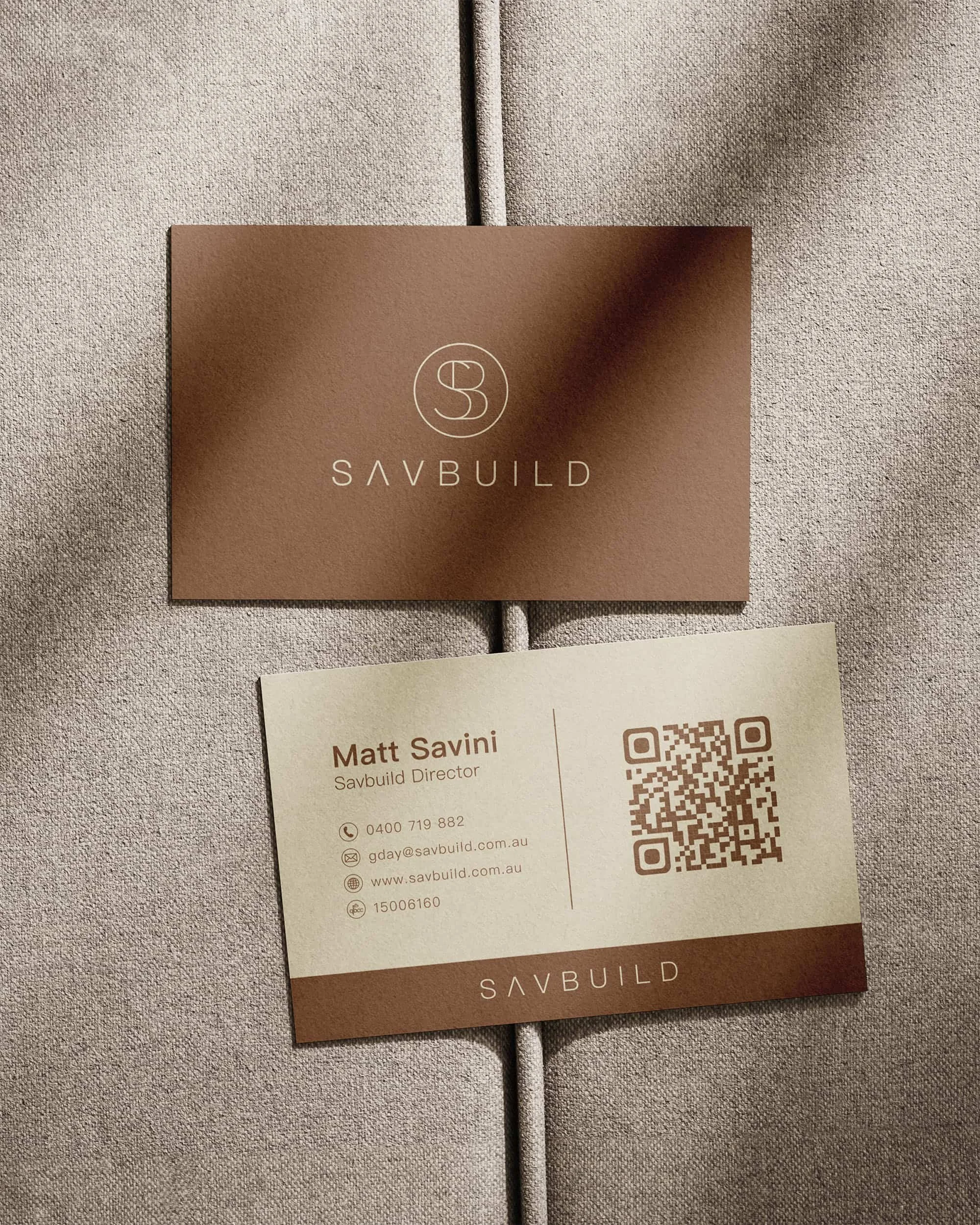 Business card and envelope for Savbuild on beige fabric background, with contact information for Matt Savini and a QR code.