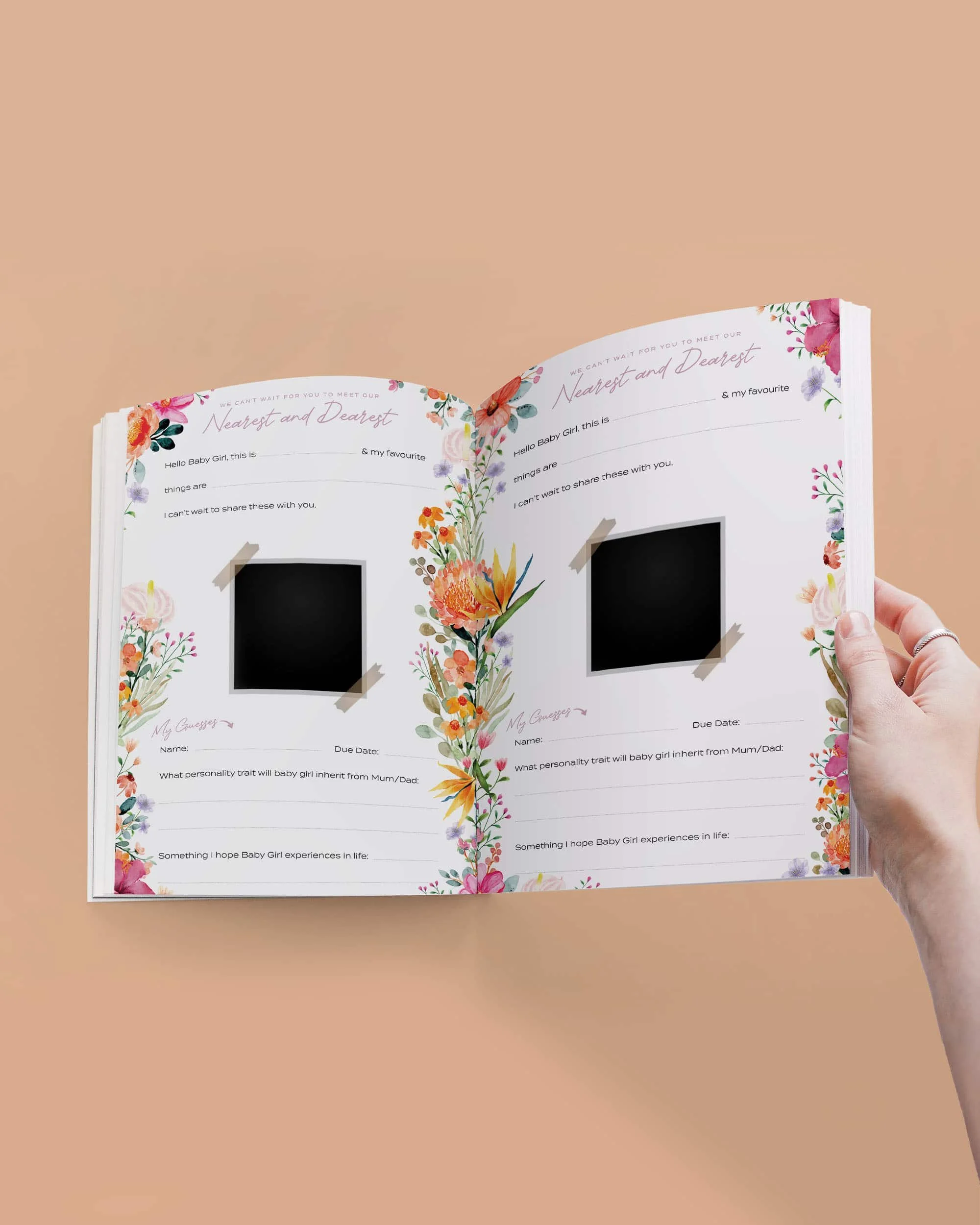 Open photo album with floral border and polaroid picture frames on pages, held by a left hand against a beige background.