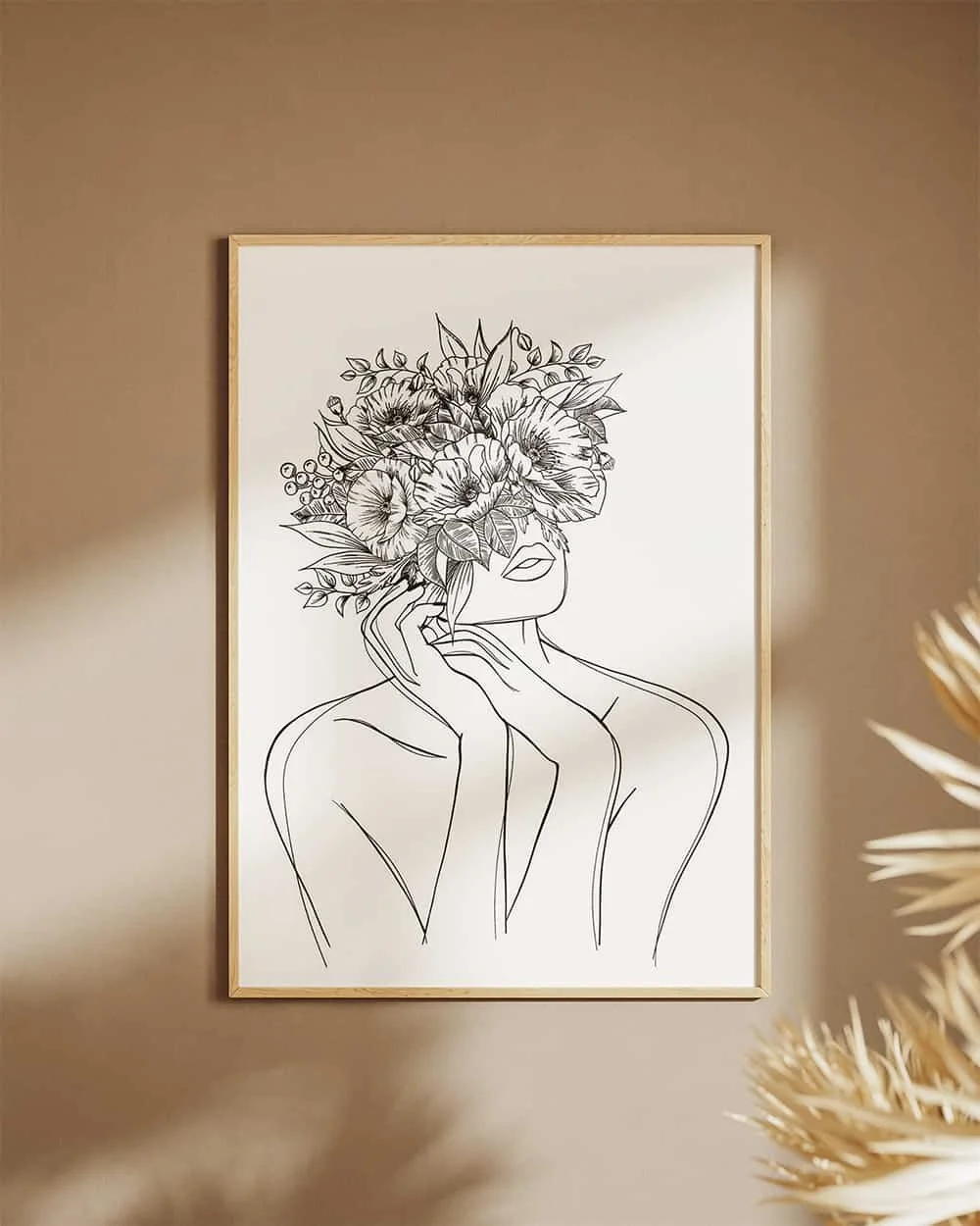 Line art illustration of a woman with flowers covering her face, framed and hanging on a beige wall.