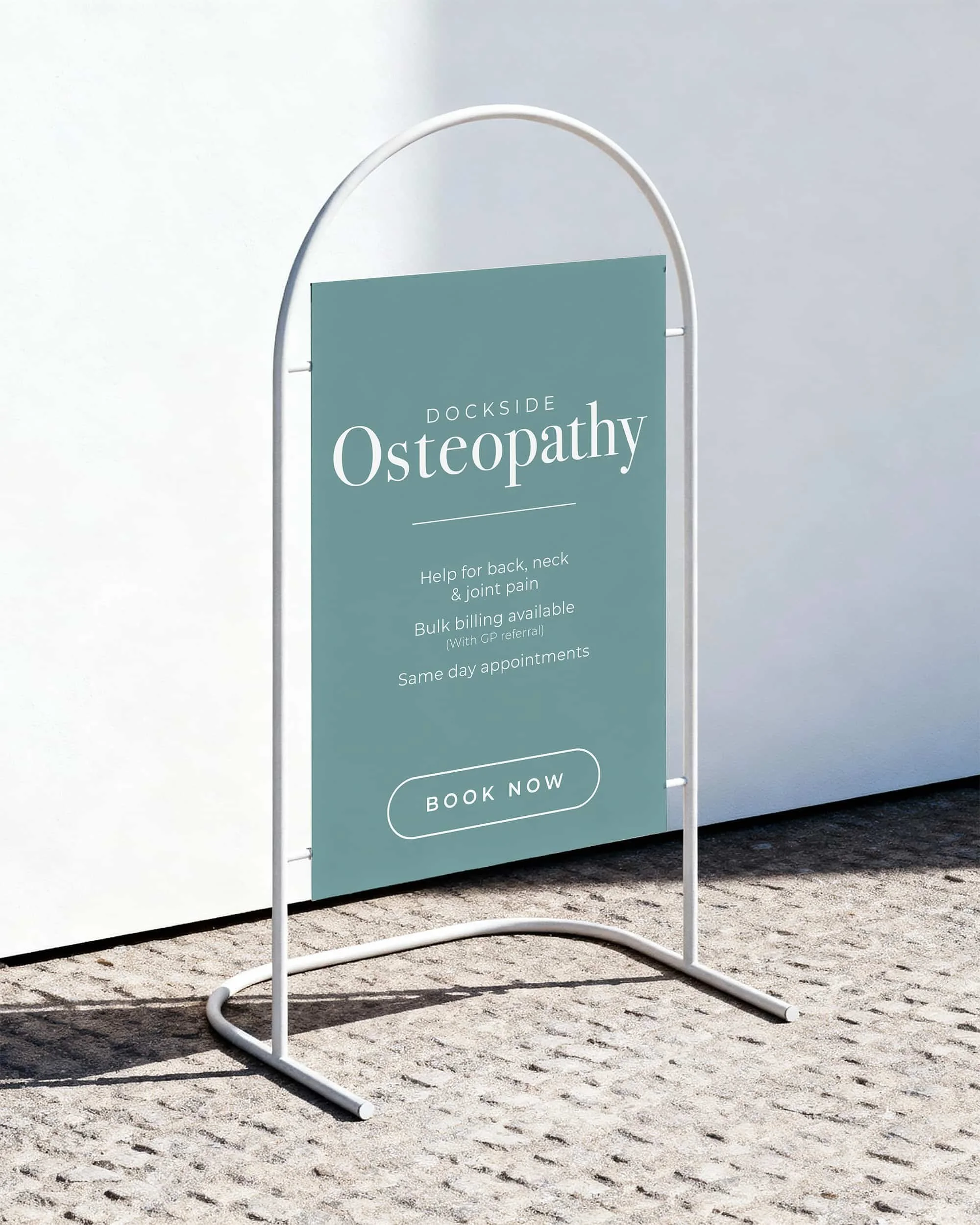 Outdoor sidewalk signboard advertising Dockside Osteopathy offering back, neck, and joint pain help, with bulk billing and same-day appointments, featuring a 'Book Now' button.