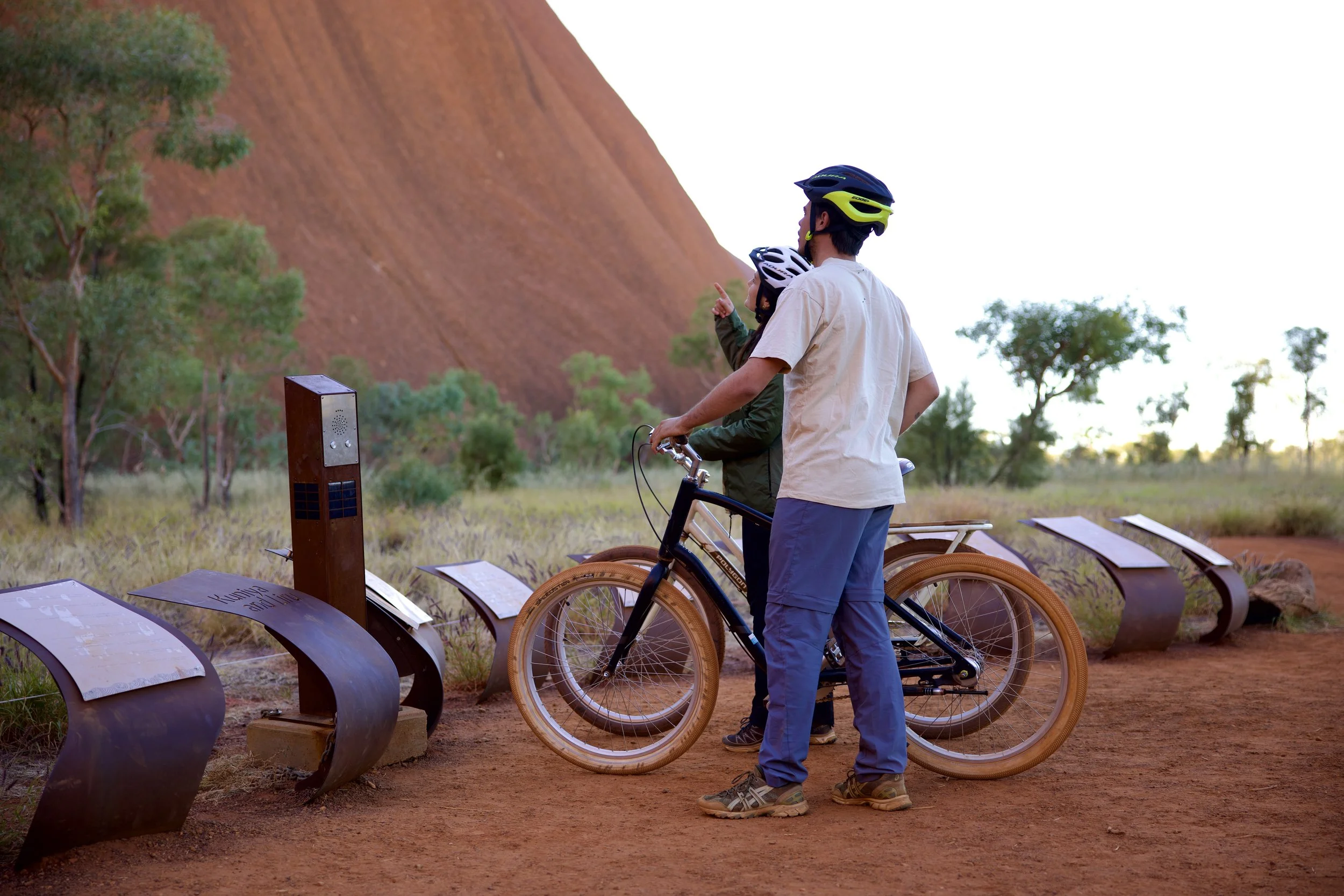 Couple with bikes reading cultural information about Uluru