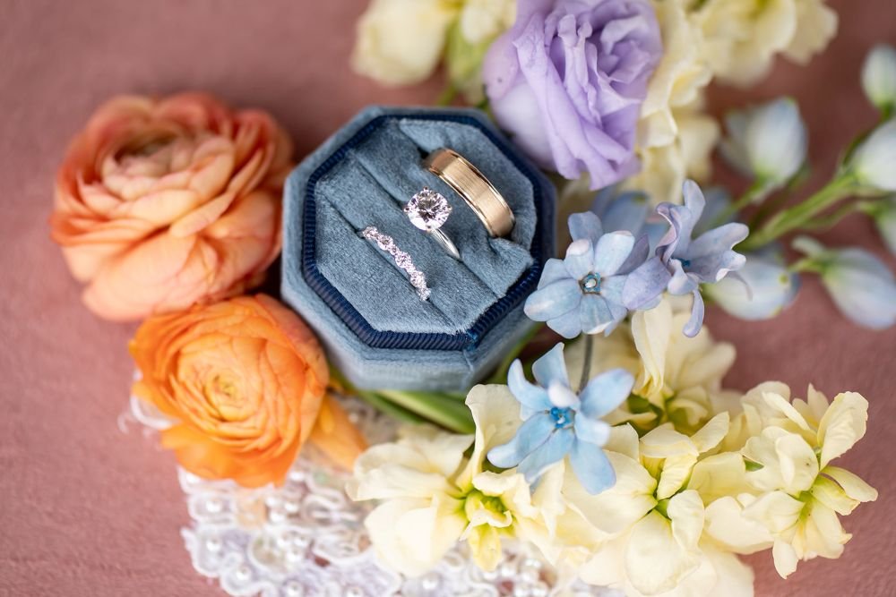 Wedding Band Set in blue ring box set amongst pastel flowers