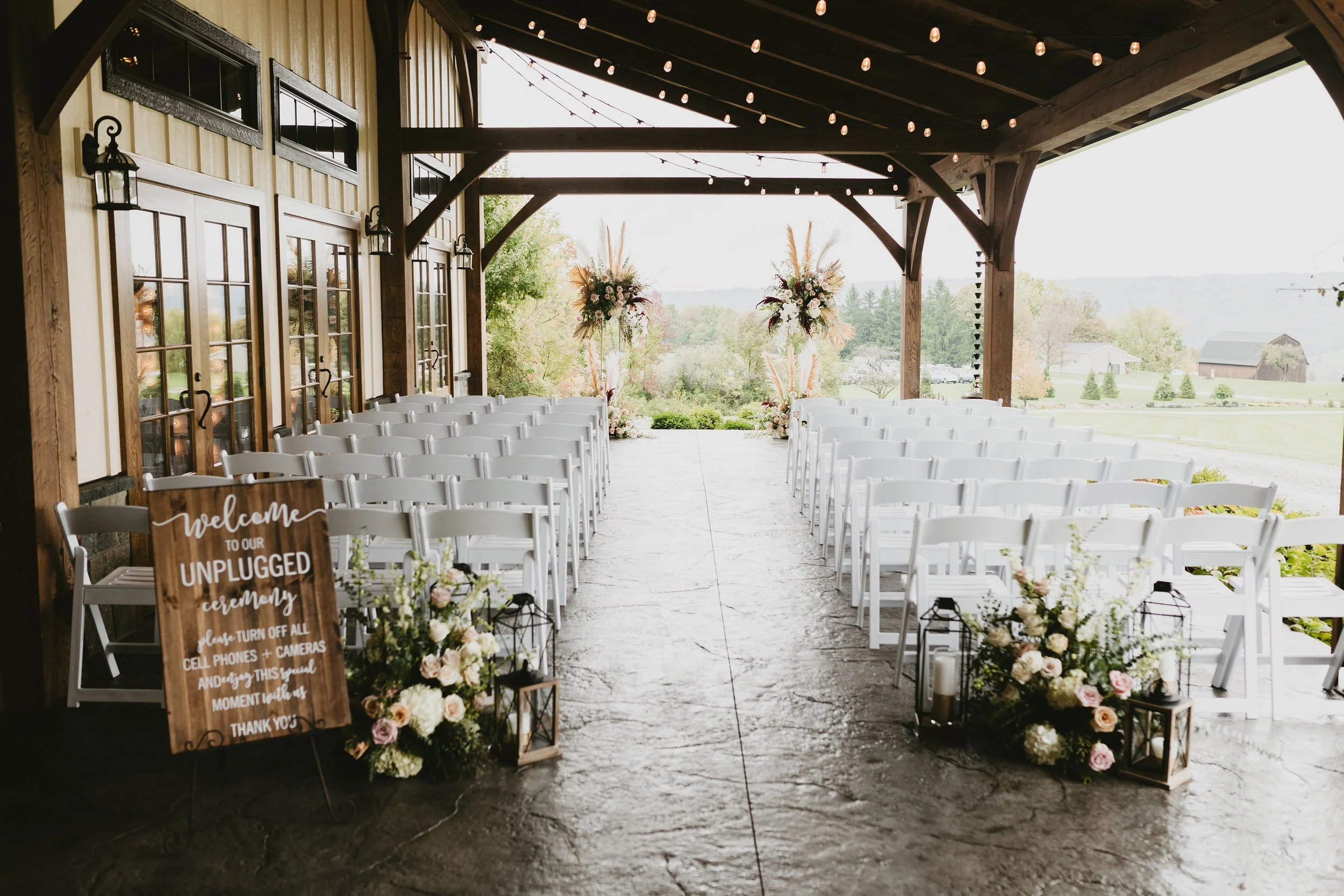 Beautiful covered wedding ceremony space with white ceremony chairs and flowers and string lights at barn wedding venue in Buffalo NY